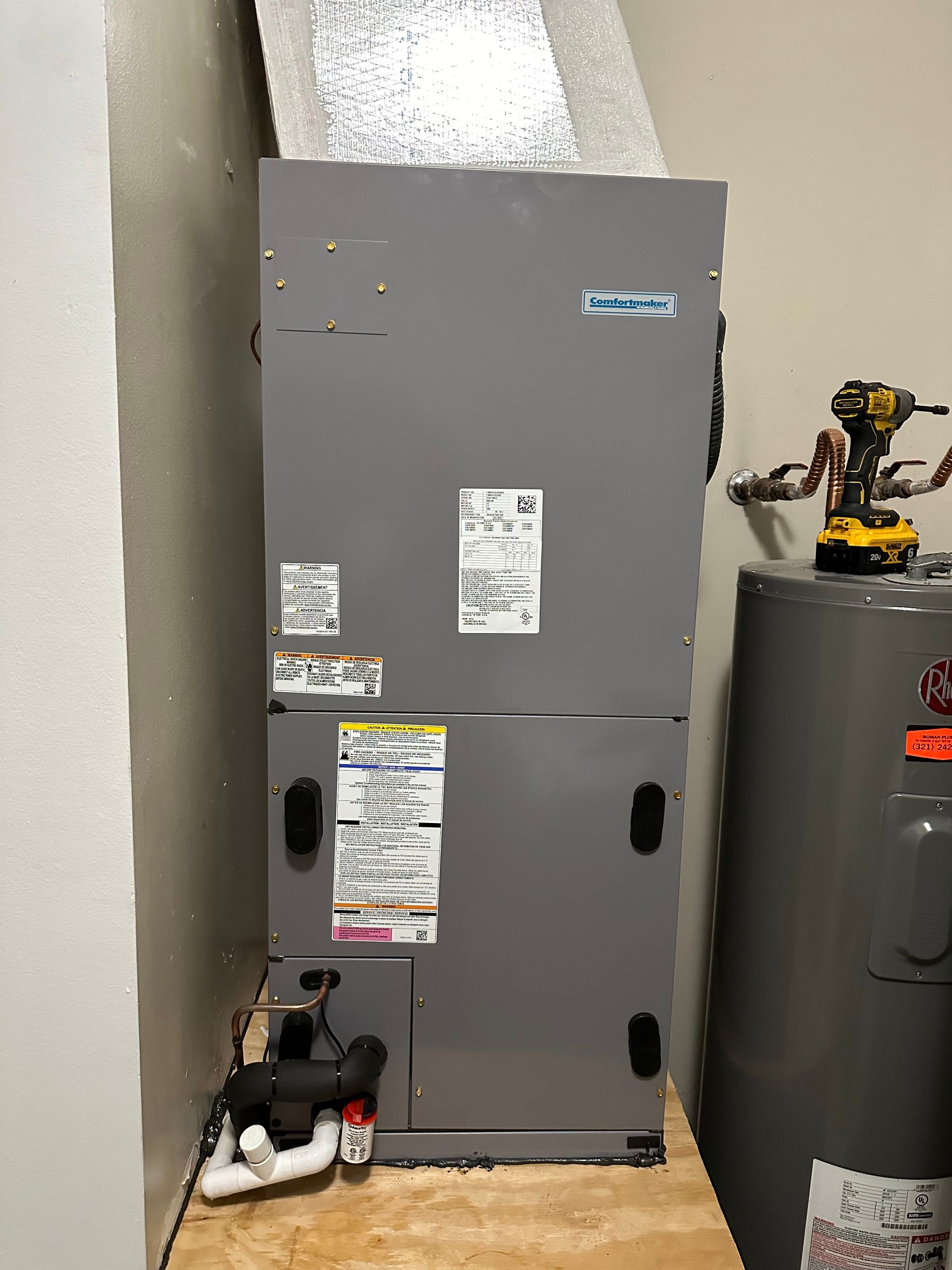 a gray air conditioner is sitting on a wooden floor next to a water heater .