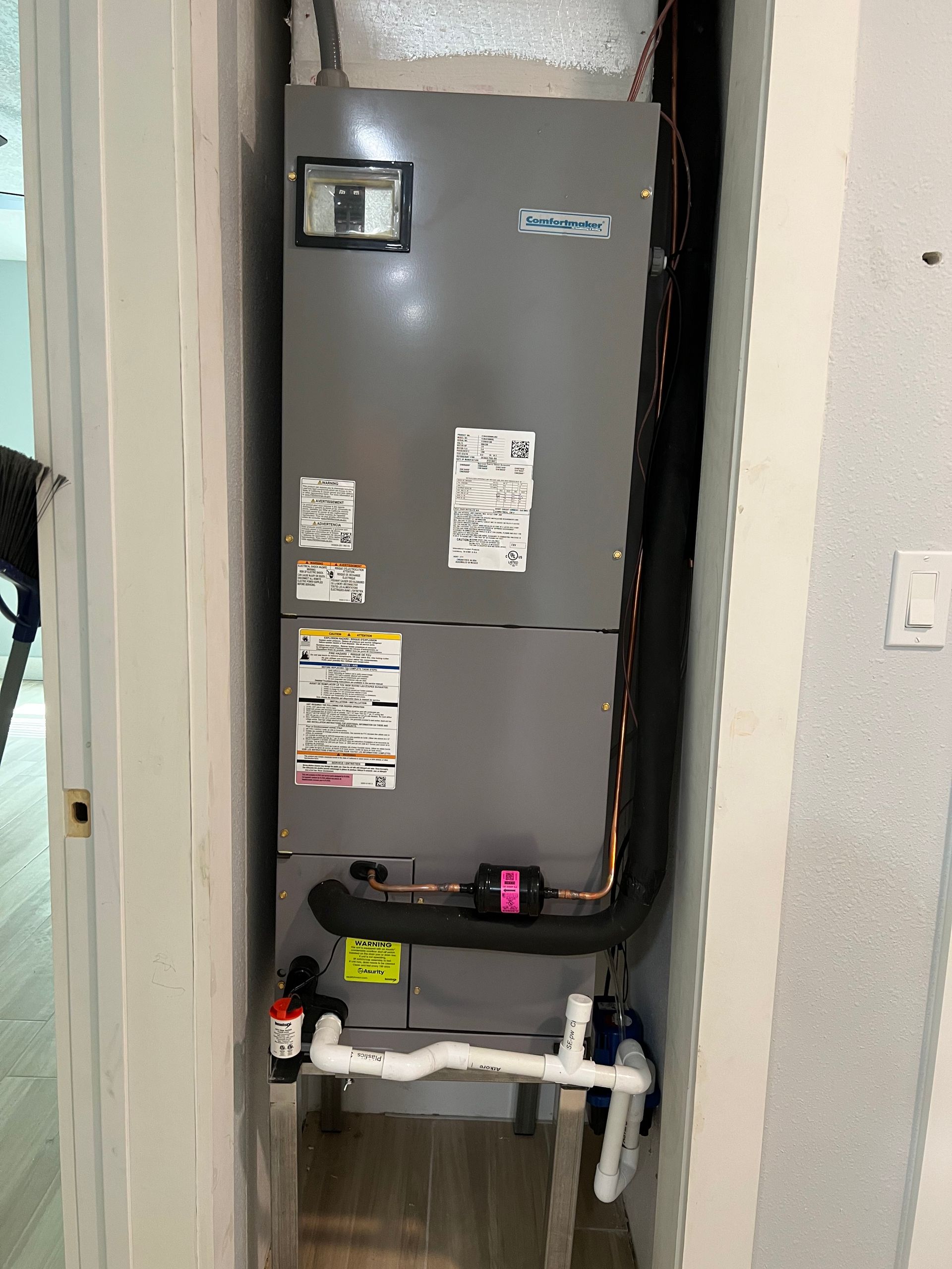 a gray air conditioner is sitting in a corner of a room next to a door .