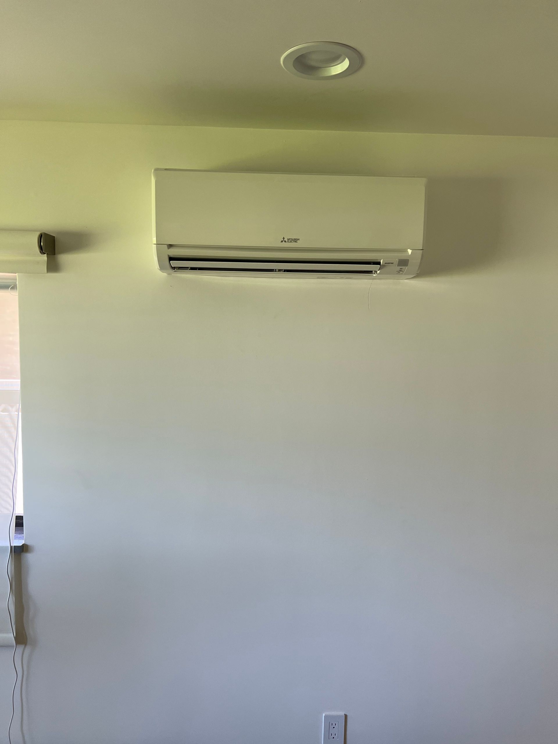 a white air conditioner is hanging on a white wall in a room .
