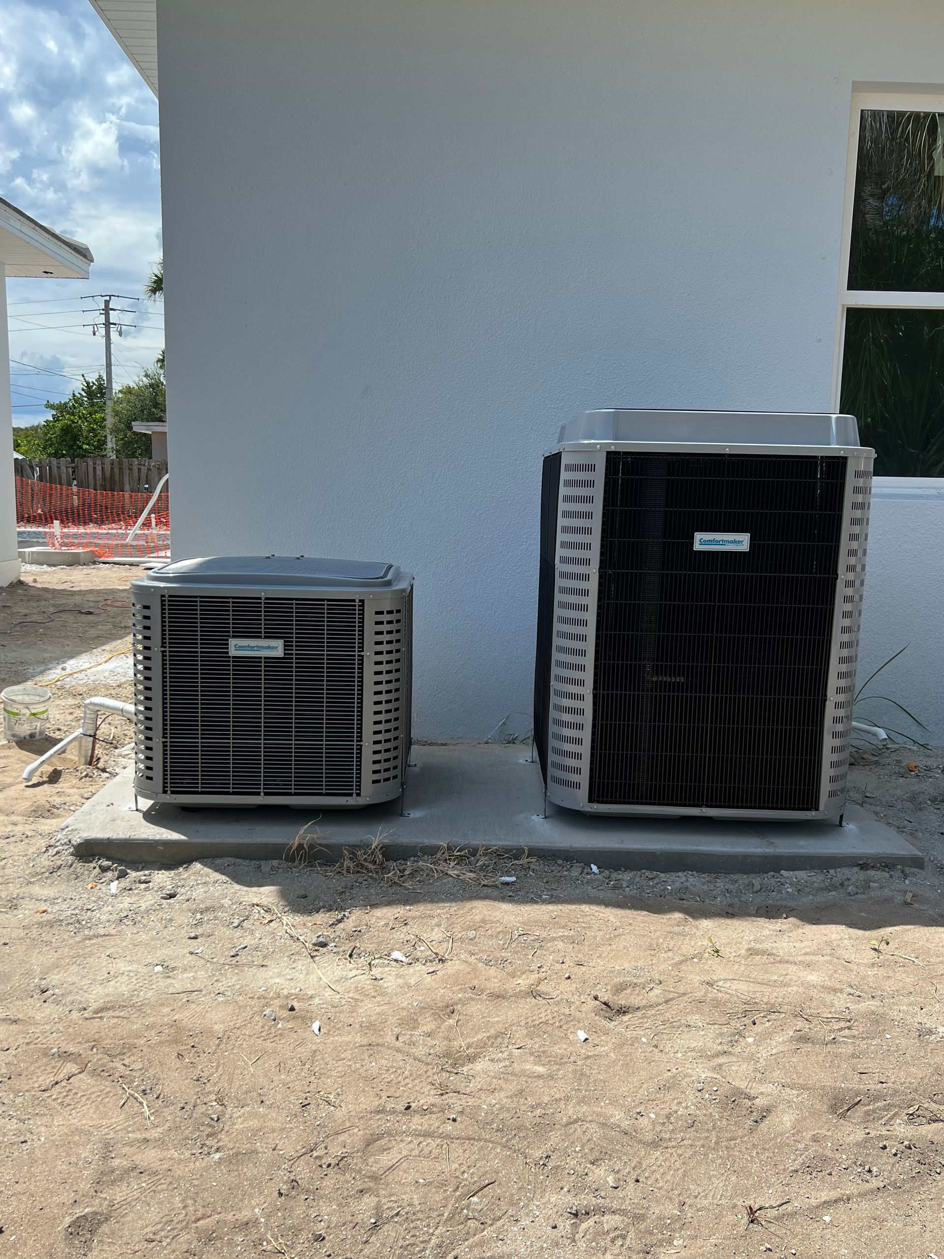two air conditioners are sitting next to each other on the side of a building .