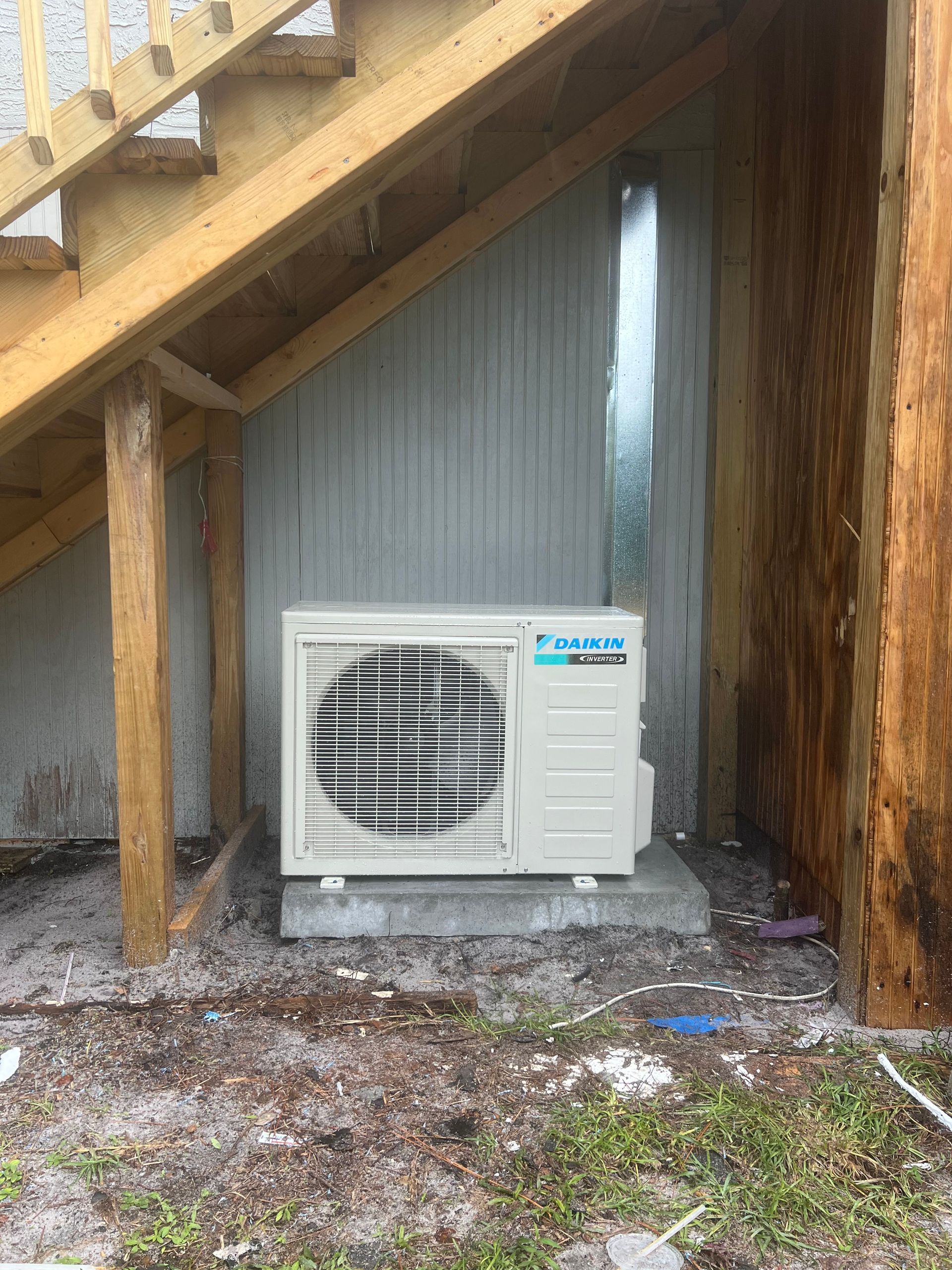 a white air conditioner is sitting under a set of stairs .