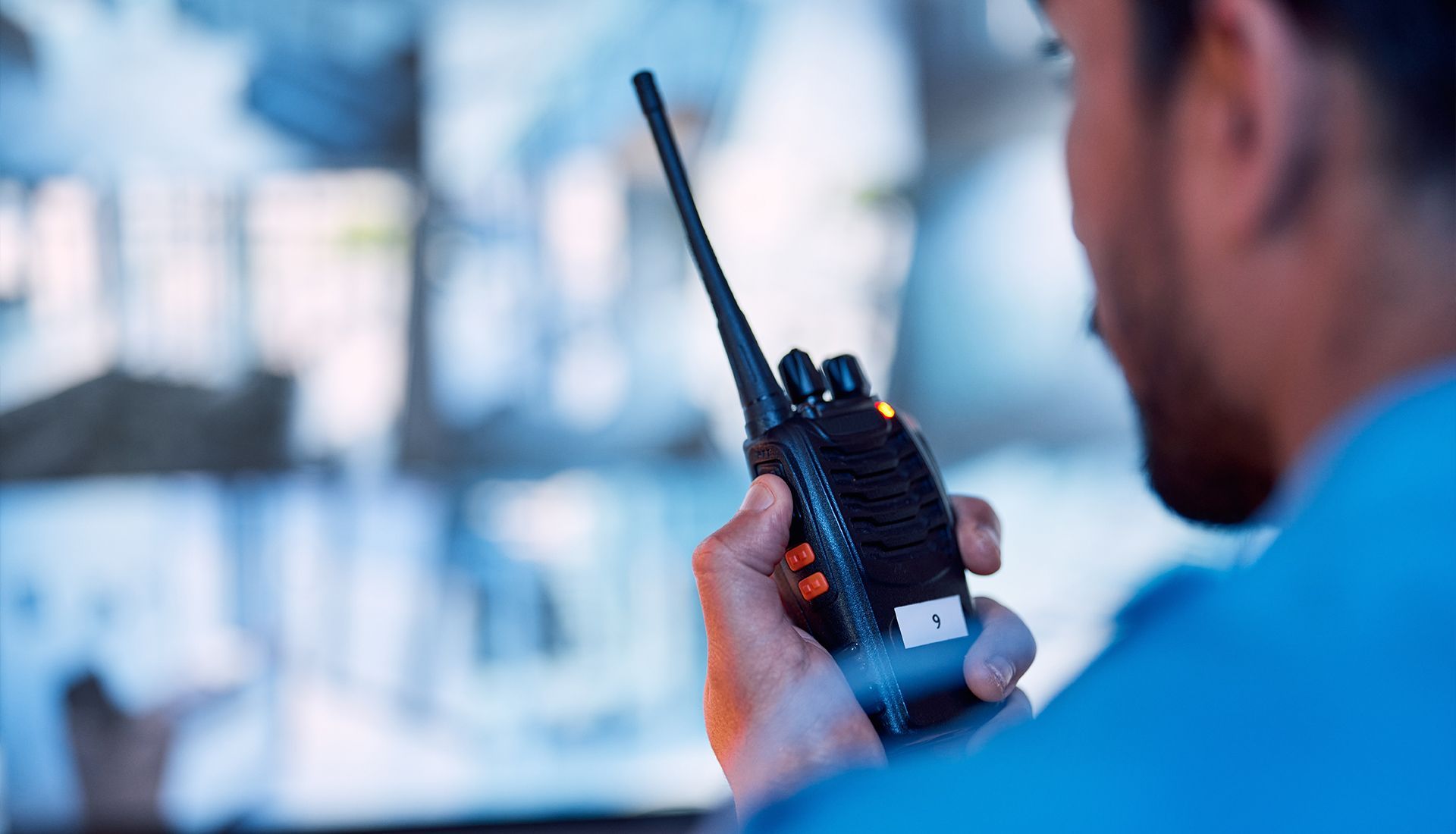 Person holding a walkie-talkie, looking at security camera monitors.