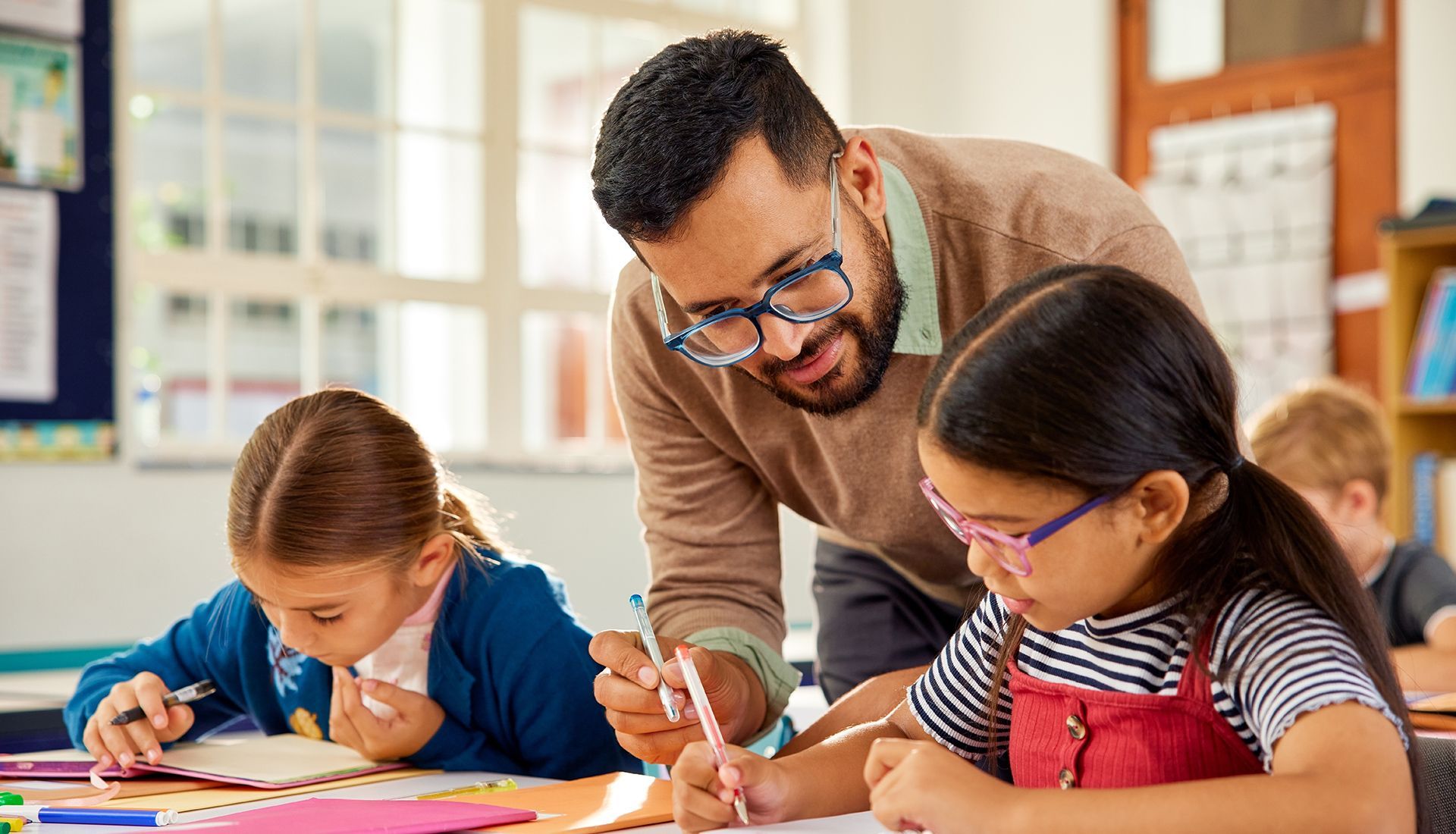 Teacher assisting students at desks; classroom setting.