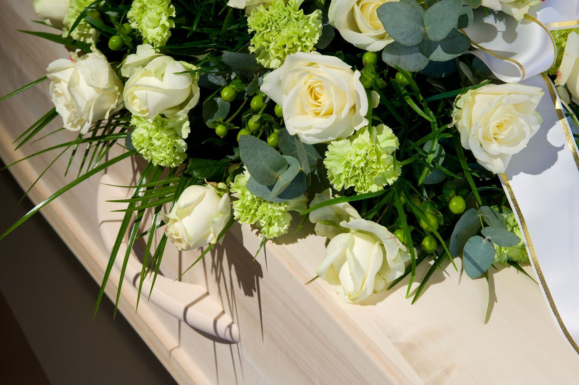 A coffin with white roses and green carnations on it.