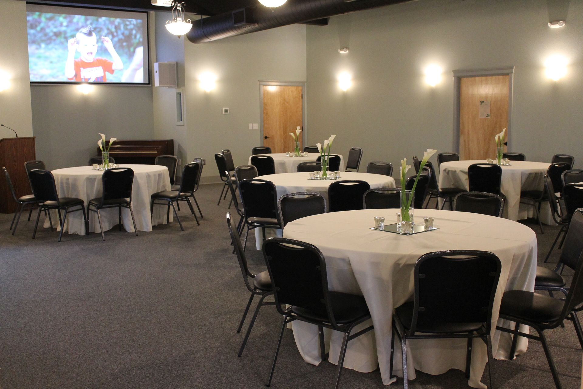 A room with tables and chairs and a projector screen