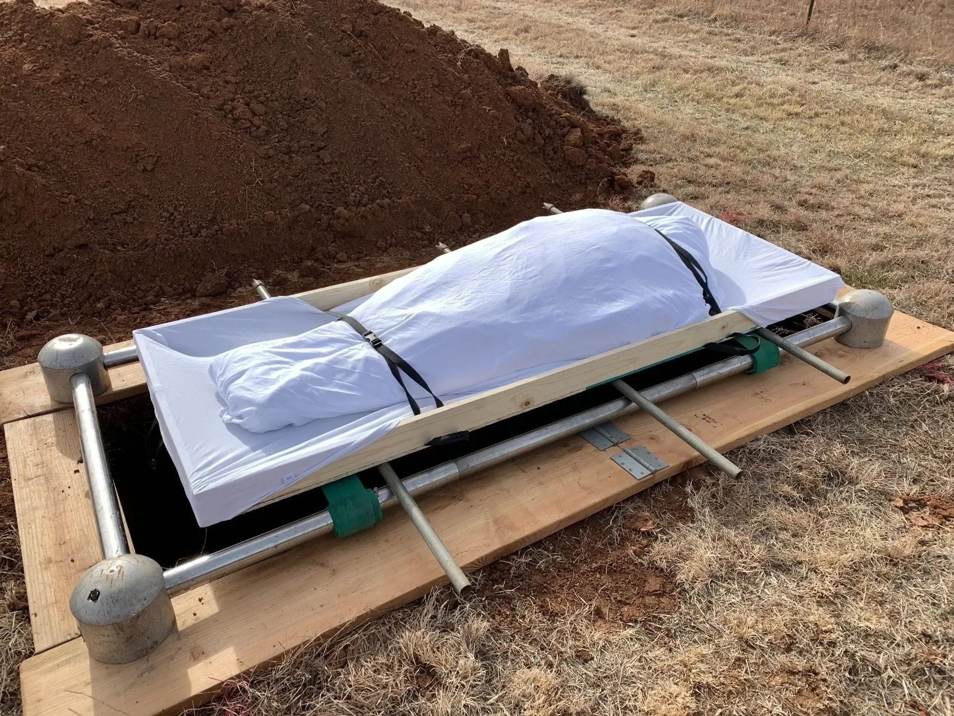 White-covered object strapped to a wooden pallet outdoors on a dirt patch