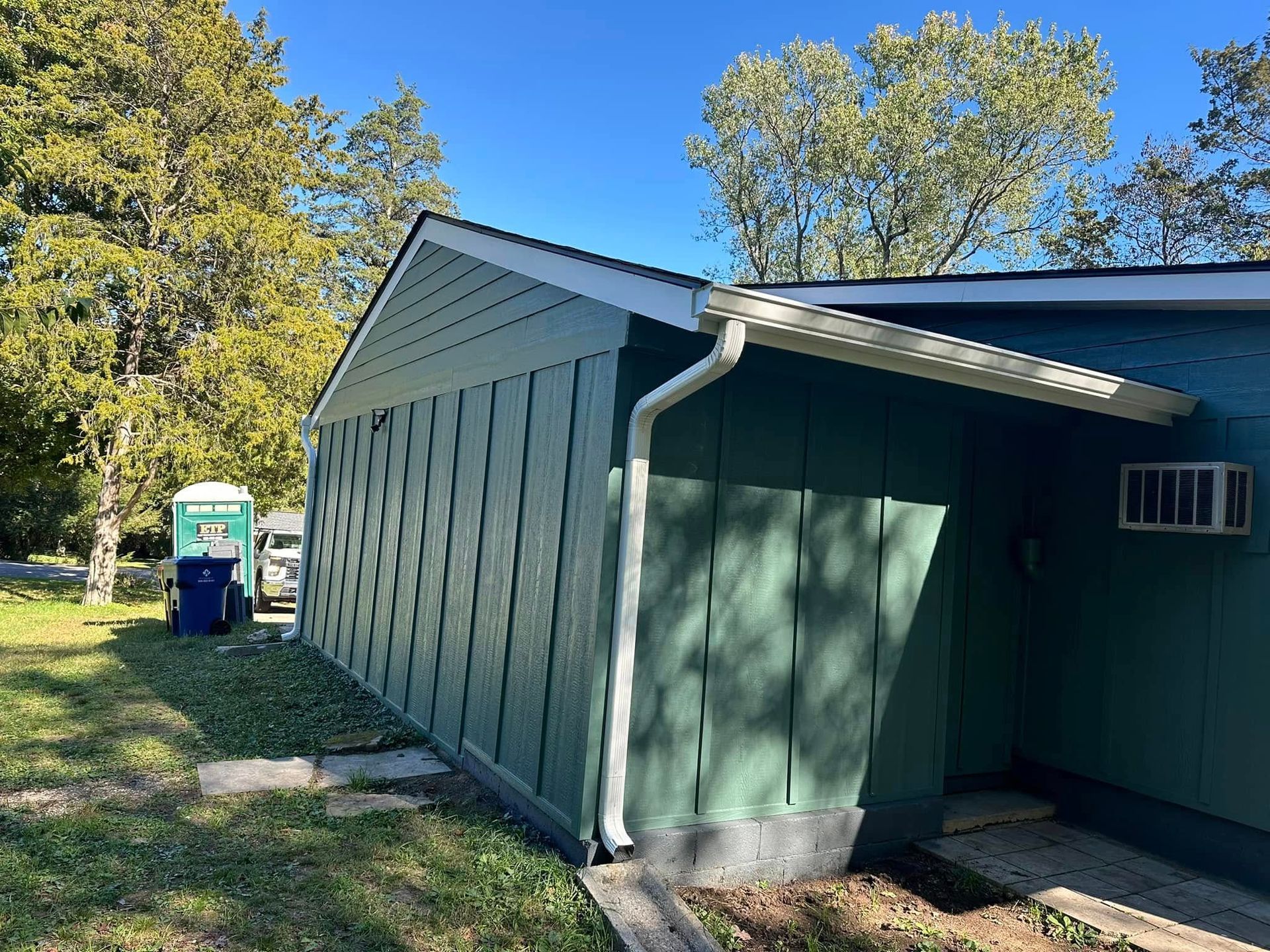 A green house with a white gutter on the side of it.