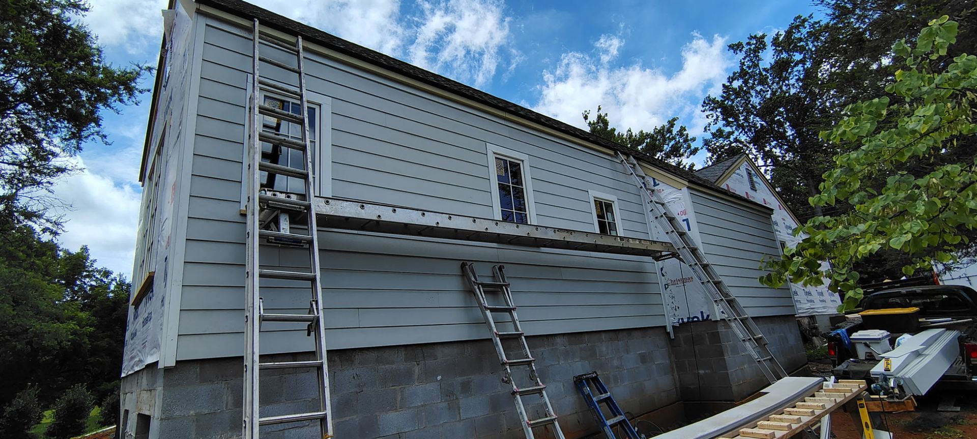 A white house is being painted with a ladder on the side of it.