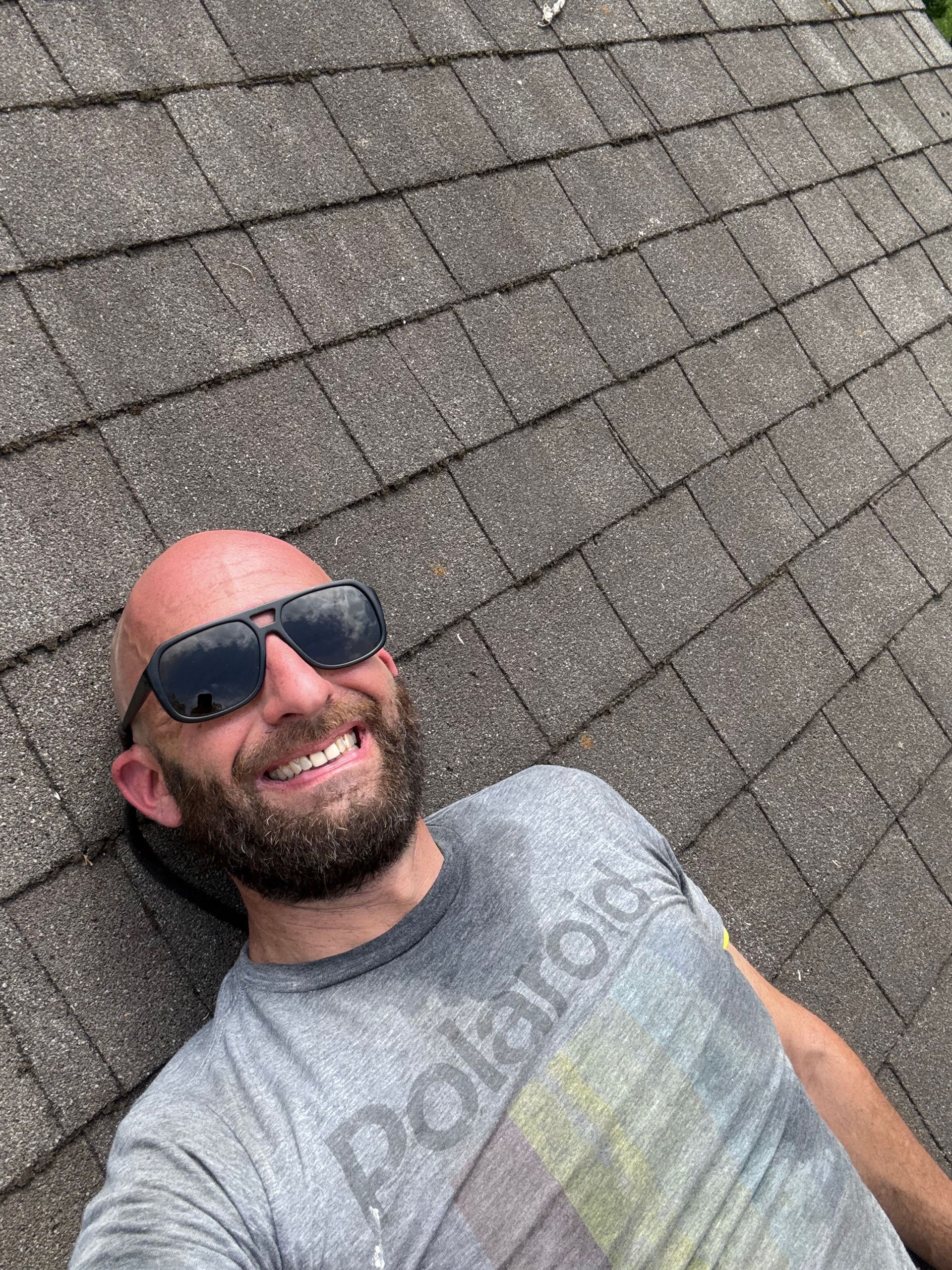 A bald man with a beard and sunglasses is laying on a roof.