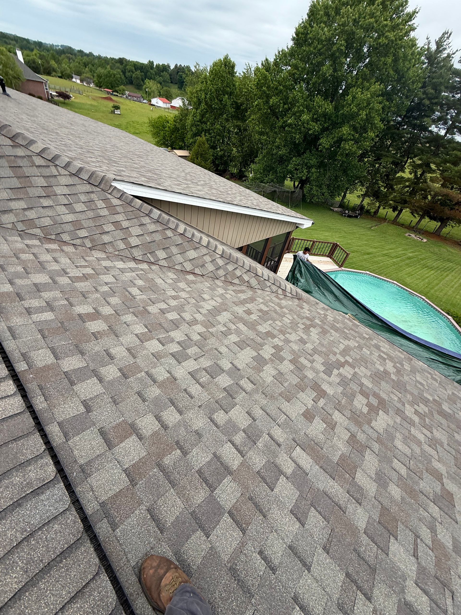 A person is standing on the roof of a house next to a pool.