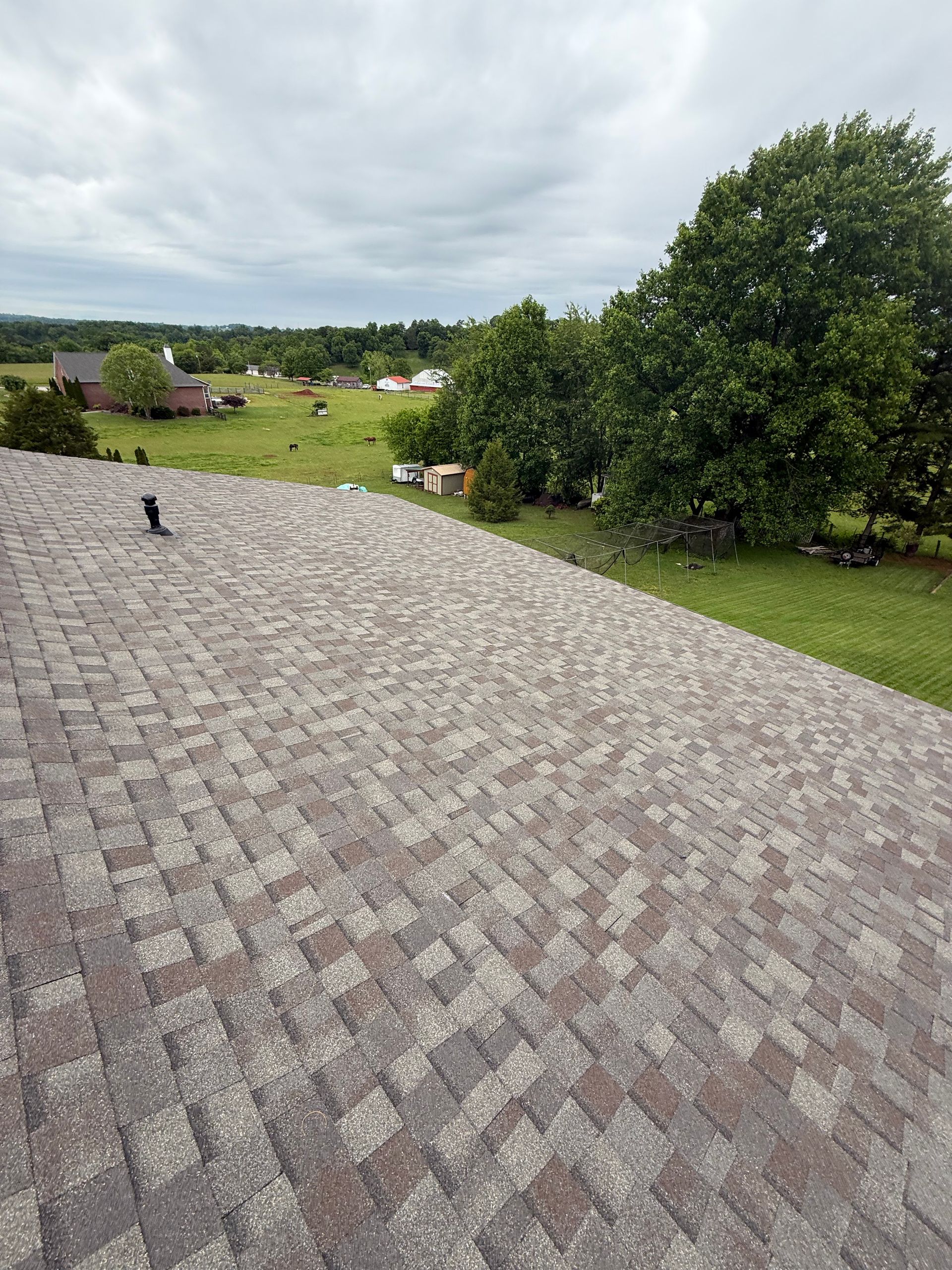 A roof with a view of a field and trees on a cloudy day.