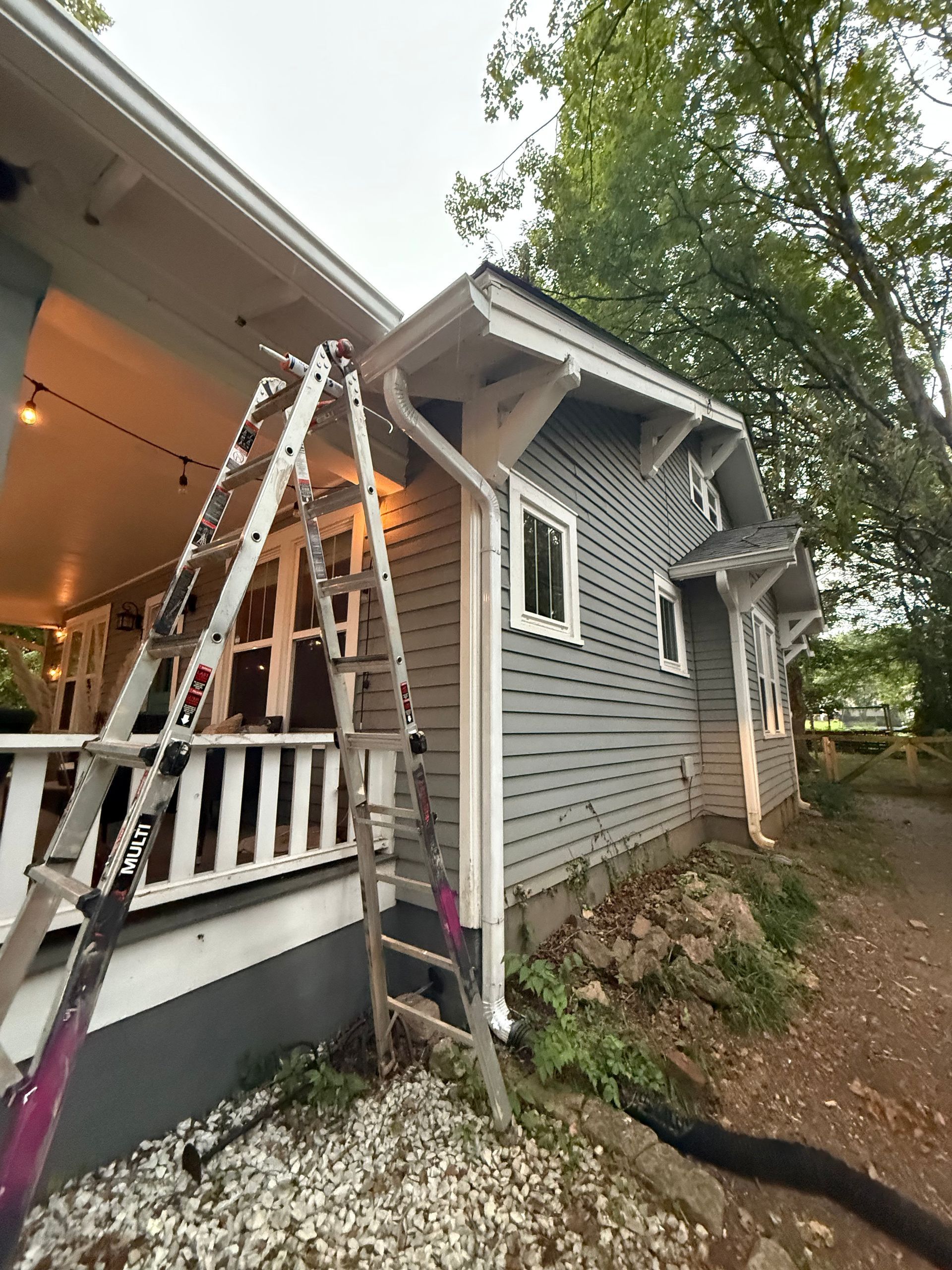 A ladder is sitting on the side of a house next to a porch.