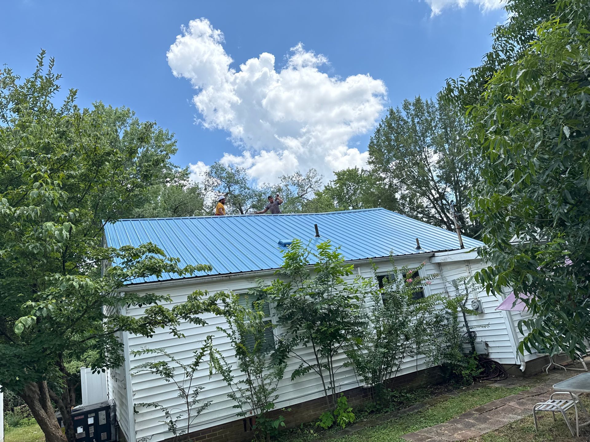 A blue metal roof is being installed on a white house.