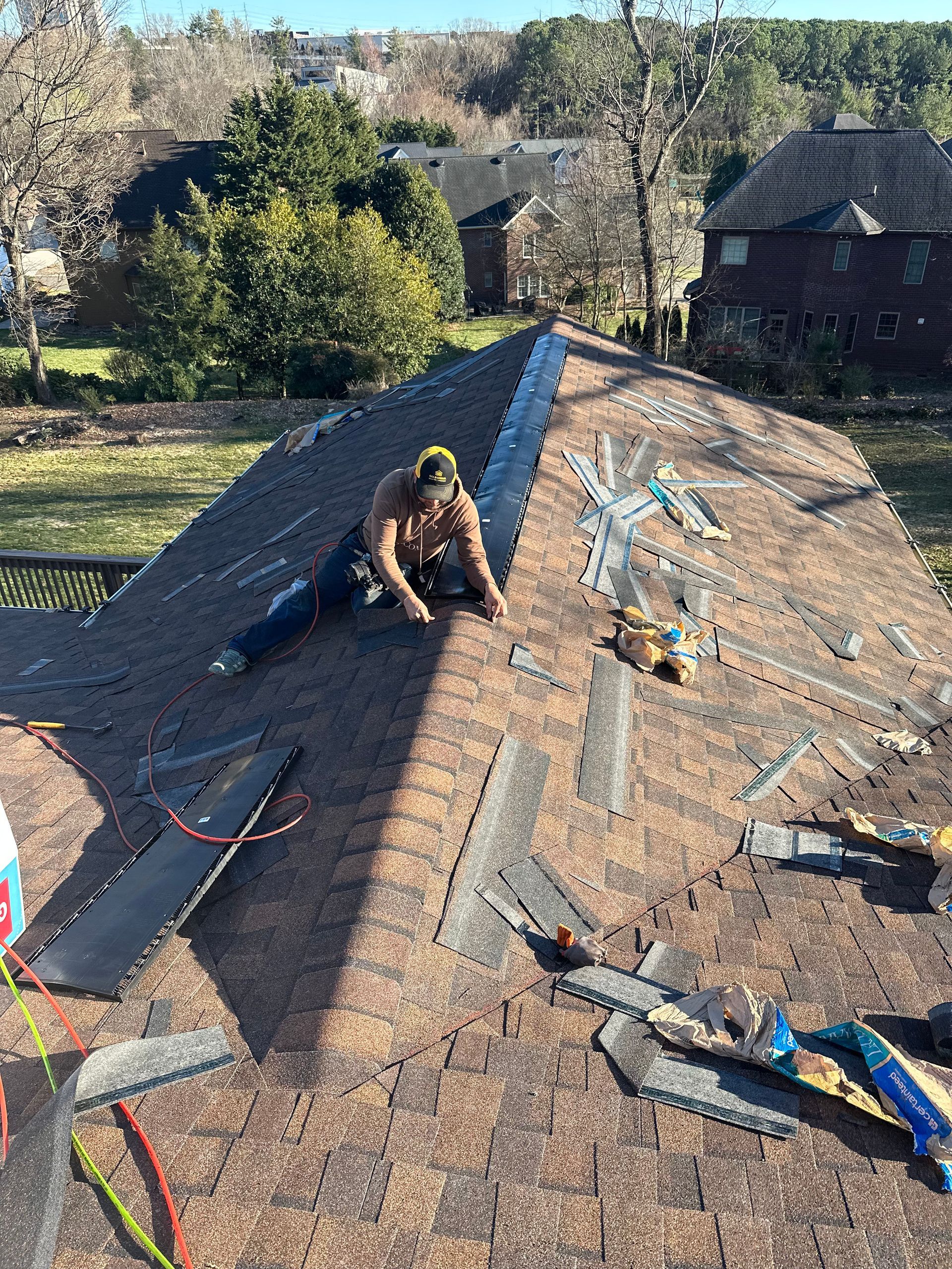 A man is sitting on top of a roof working on it.