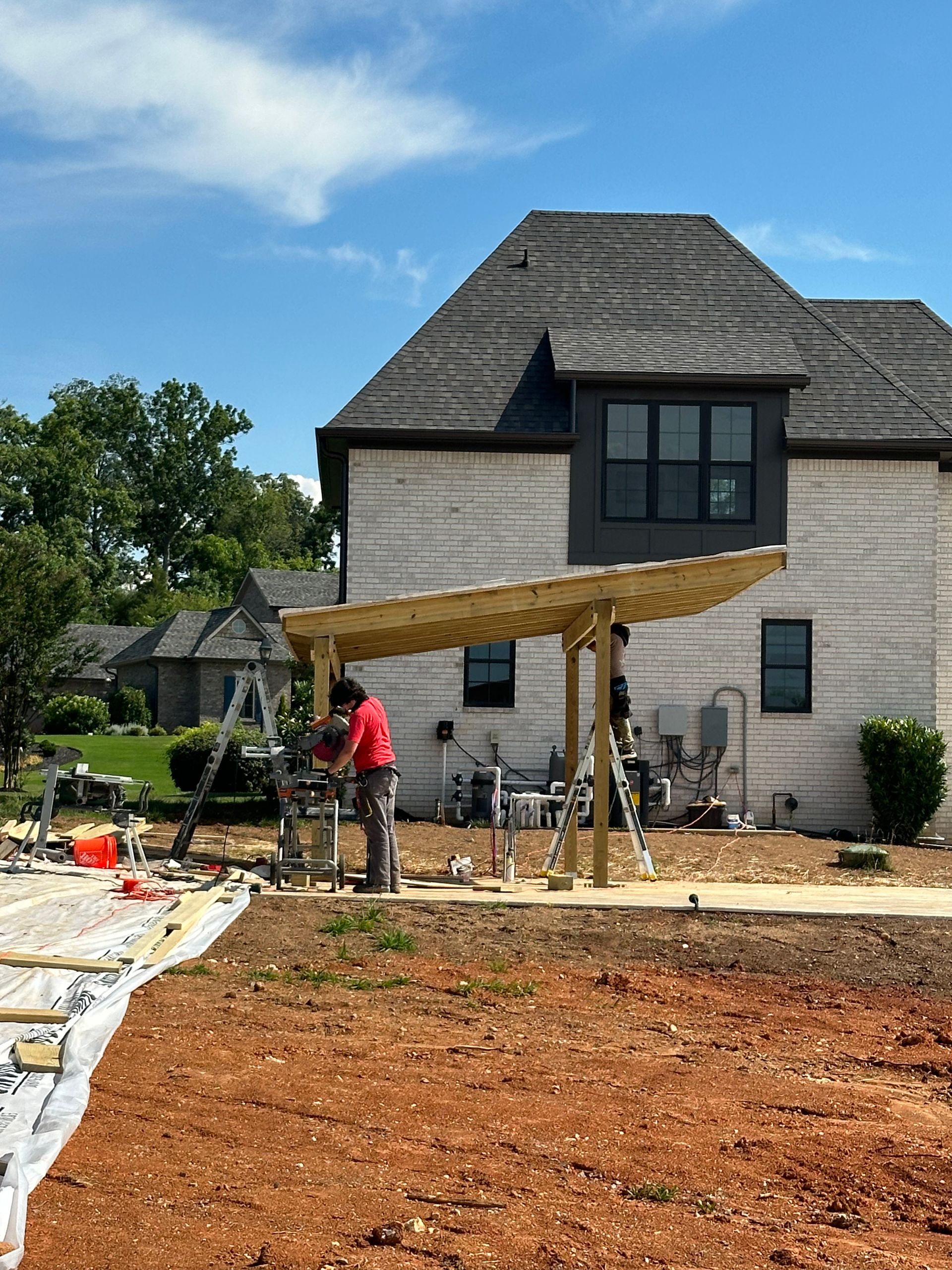 A man is working on a pergola in front of a house.