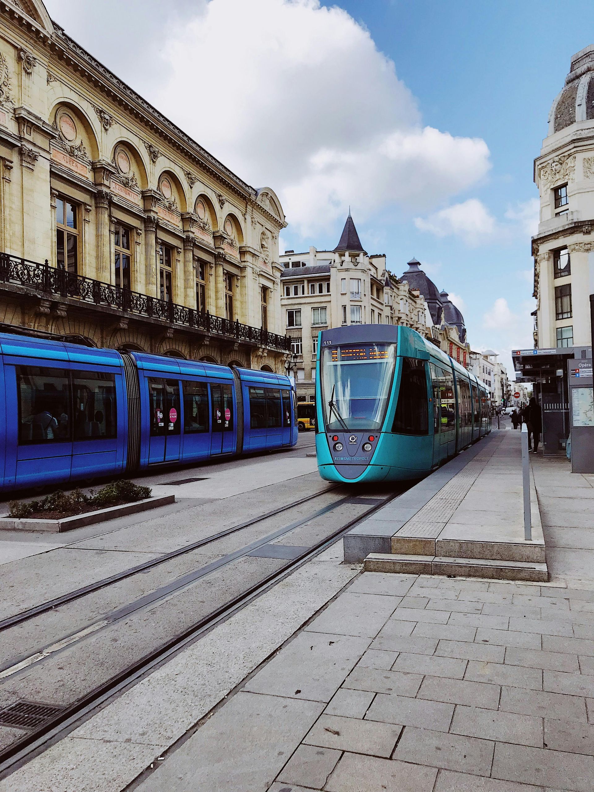 Un train bleu et vert est sur les rails devant un bâtiment à Reims