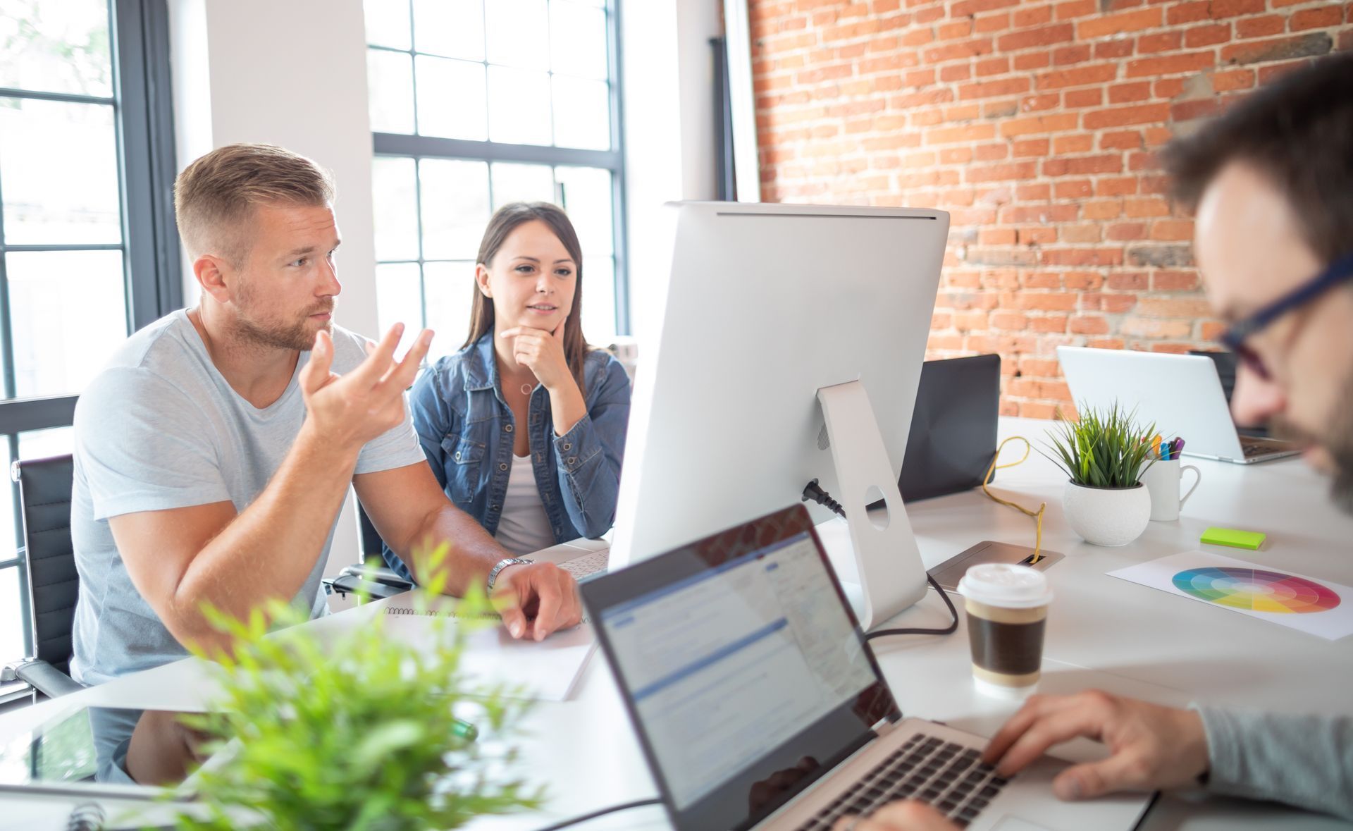 Des personnes travaillant en collaboration à des bureaux équipés d'ordinateurs, dans un bureau aux murs de briques.