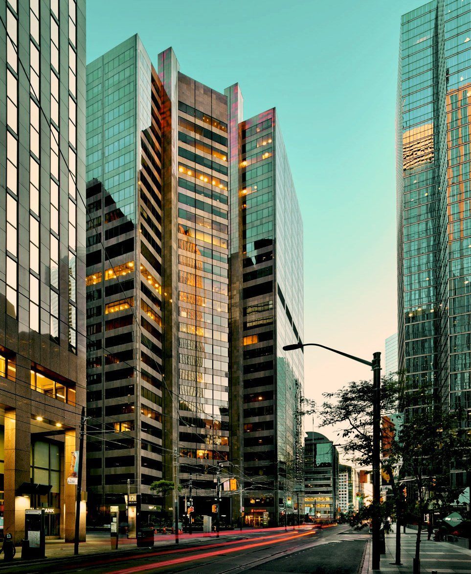Tall glass buildings line a city street; car light trails; twilight sky.