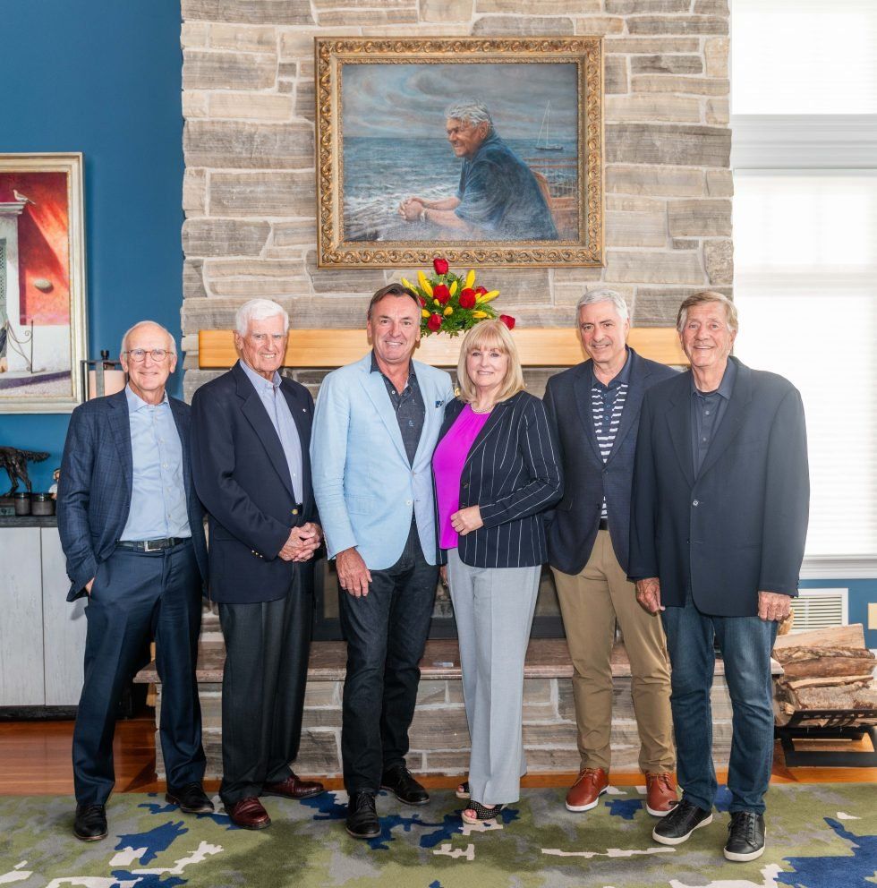 Group of six people posing in front of a fireplace and painting. 