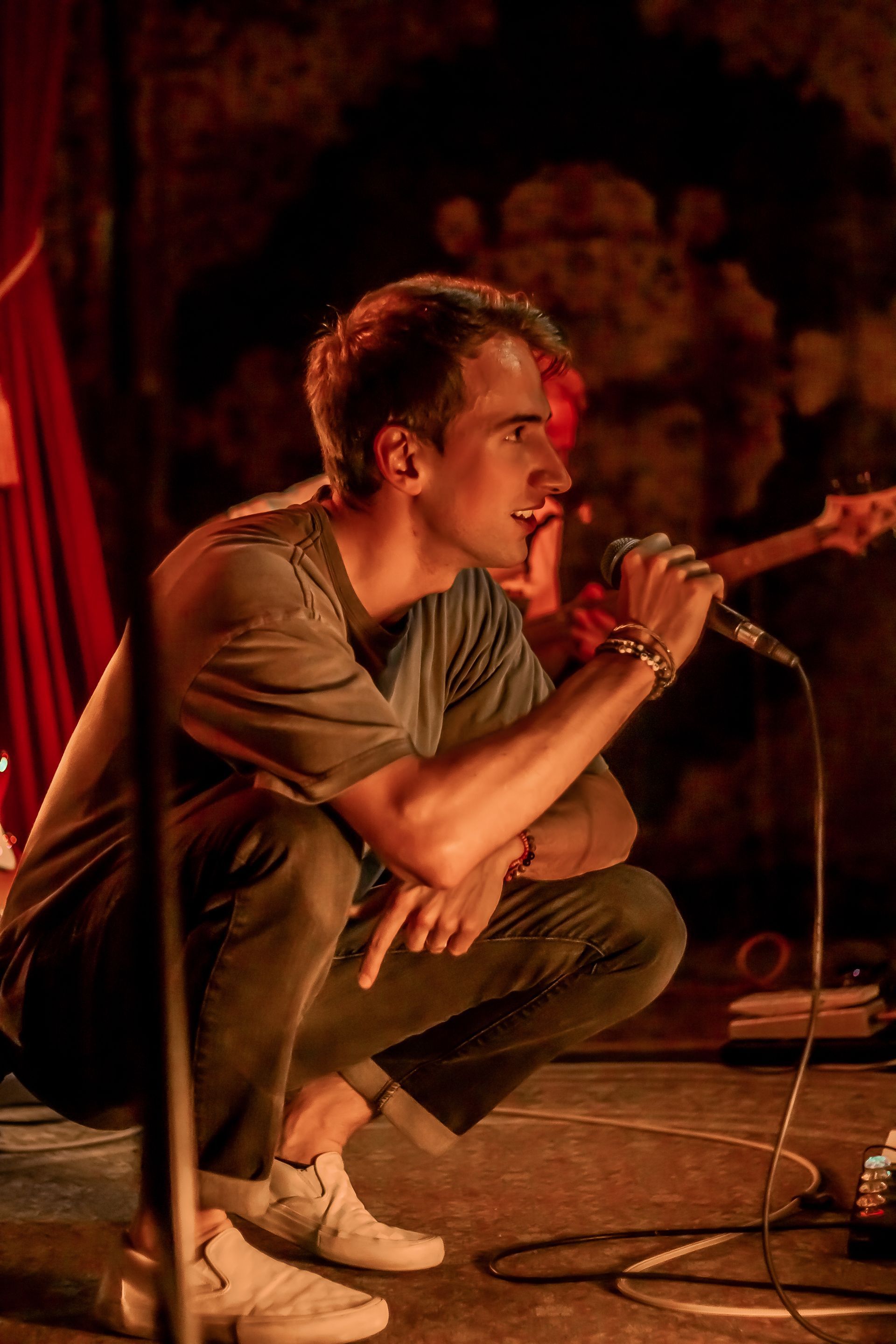 A man is kneeling down on a stage singing into a microphone.