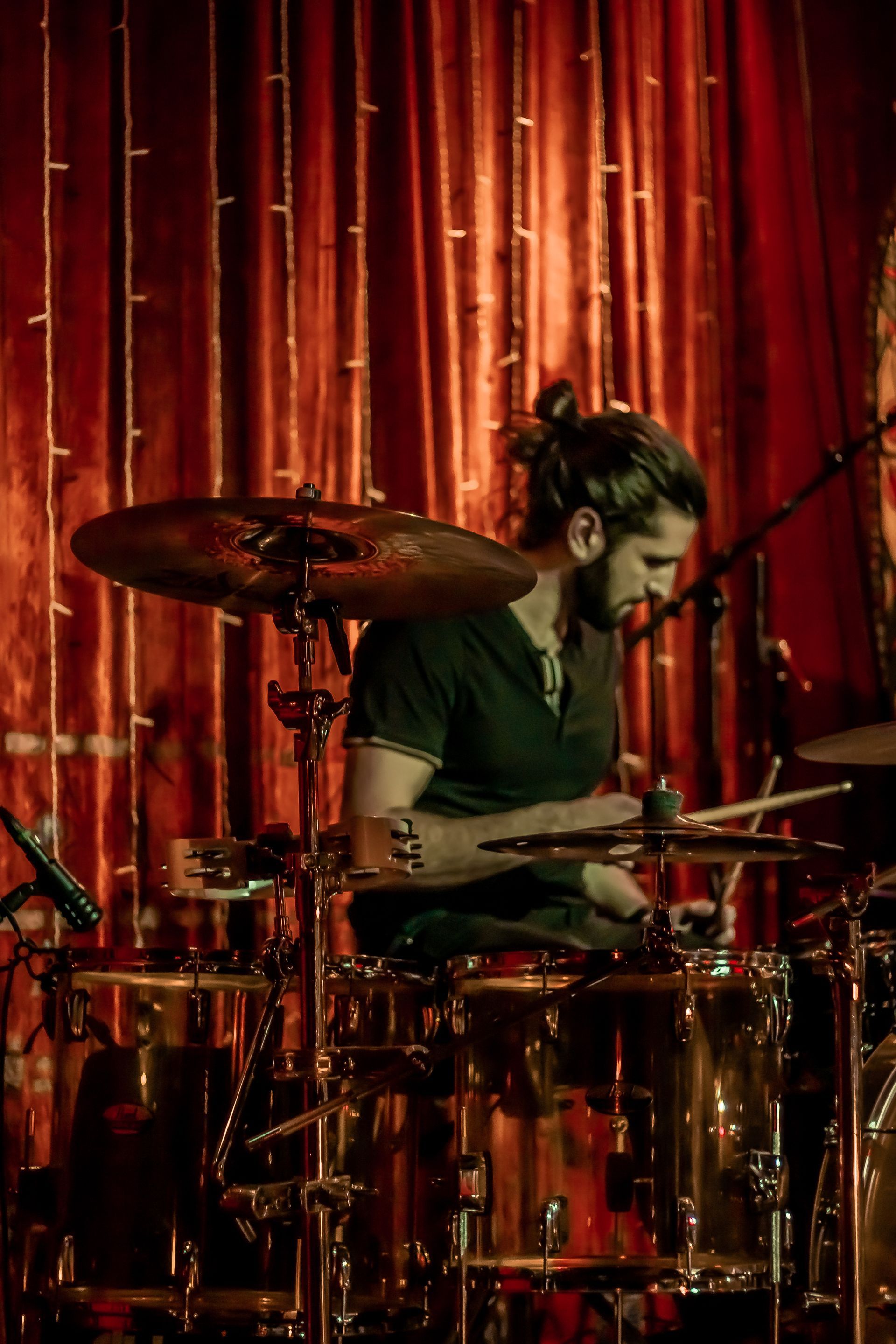 A man is playing drums on a stage in front of a red curtain.