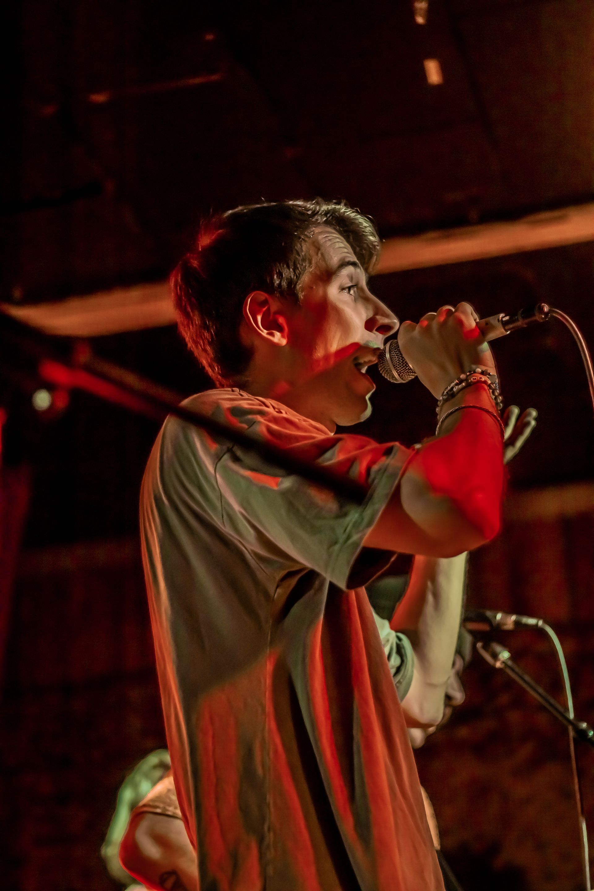 Danny from 19 Miles Per Hour is singing into a microphone on a stage in a dark room.