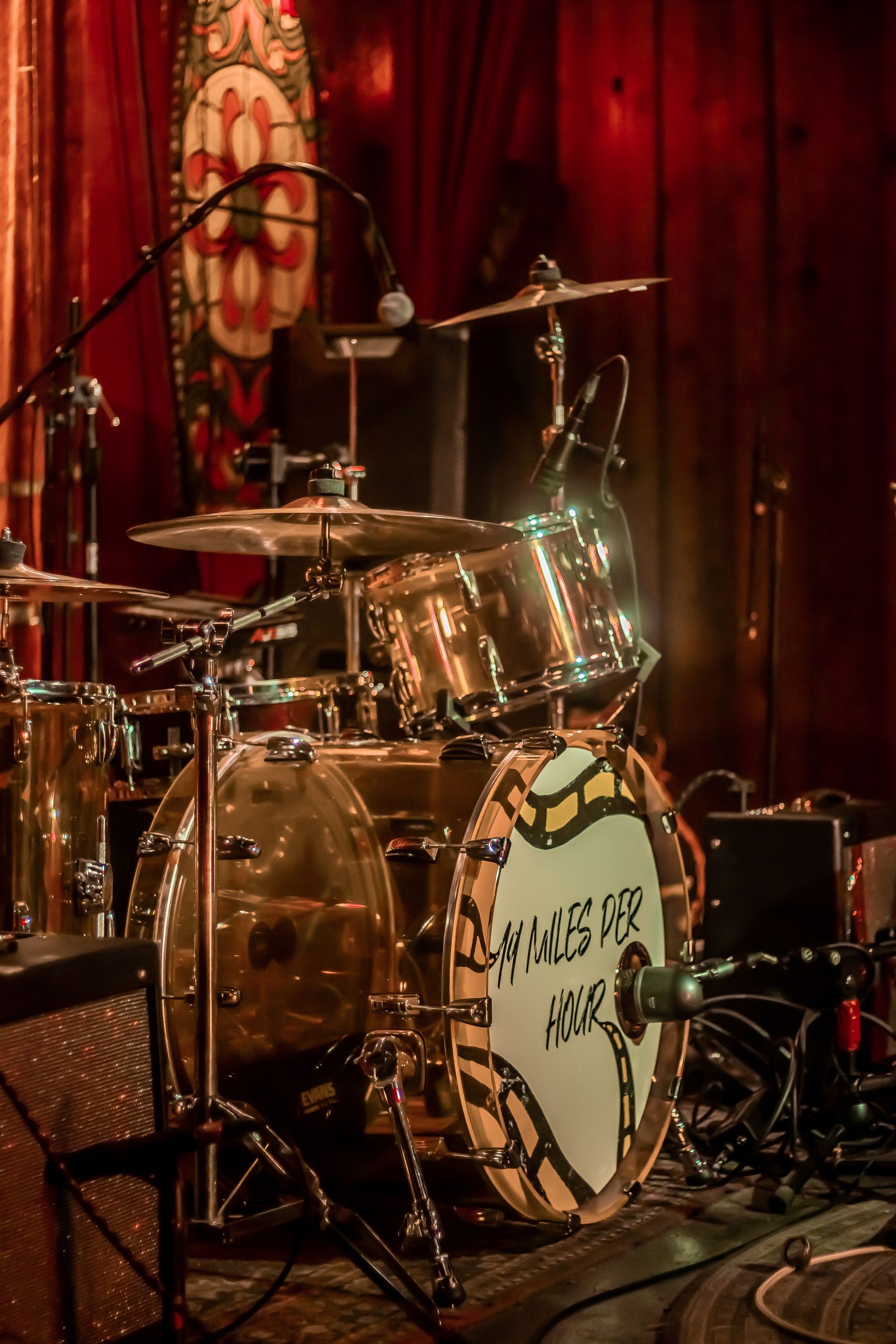 A drum set is sitting on a stage in front of a red curtain.