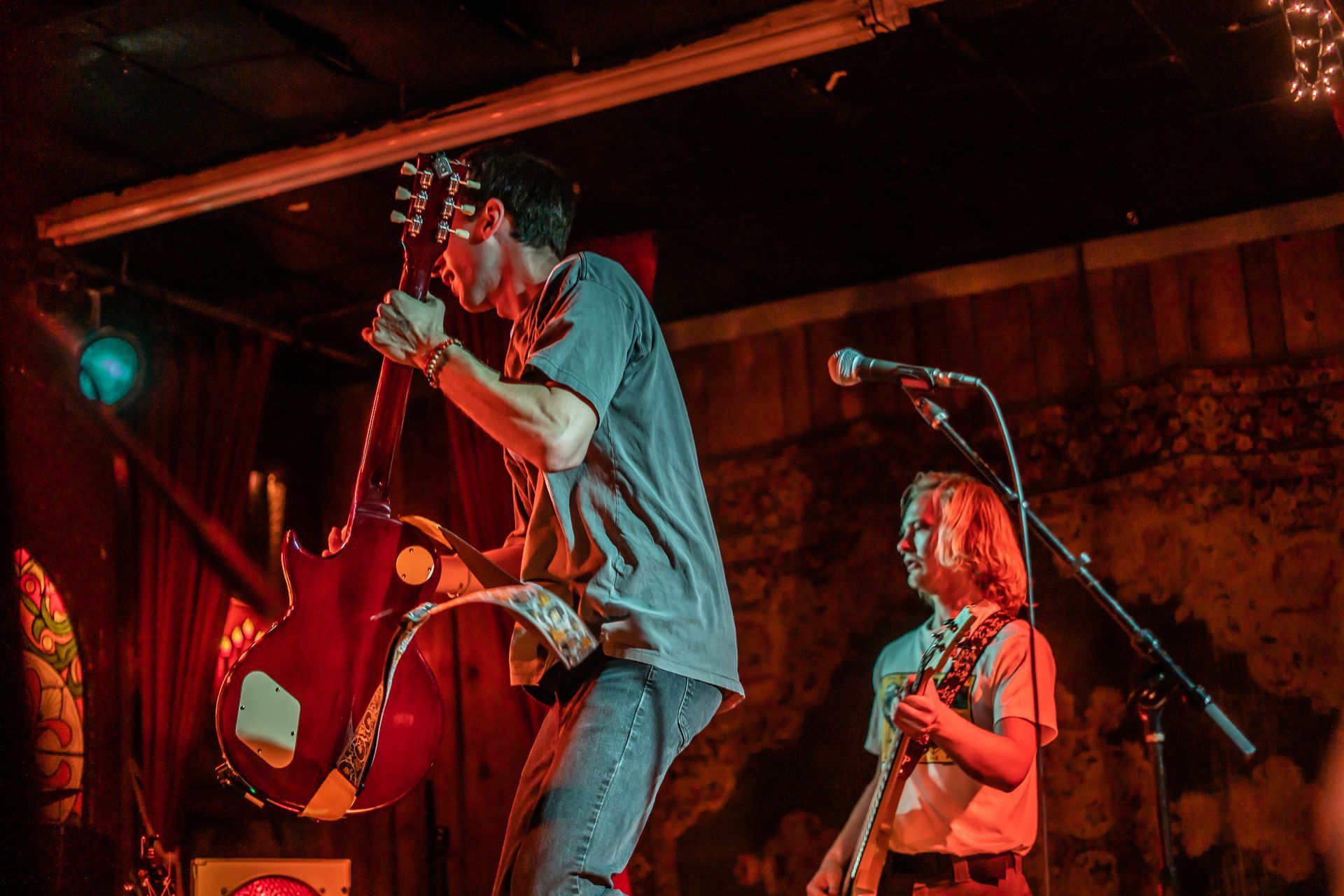 A man is playing a guitar on stage while another man sings into a microphone.