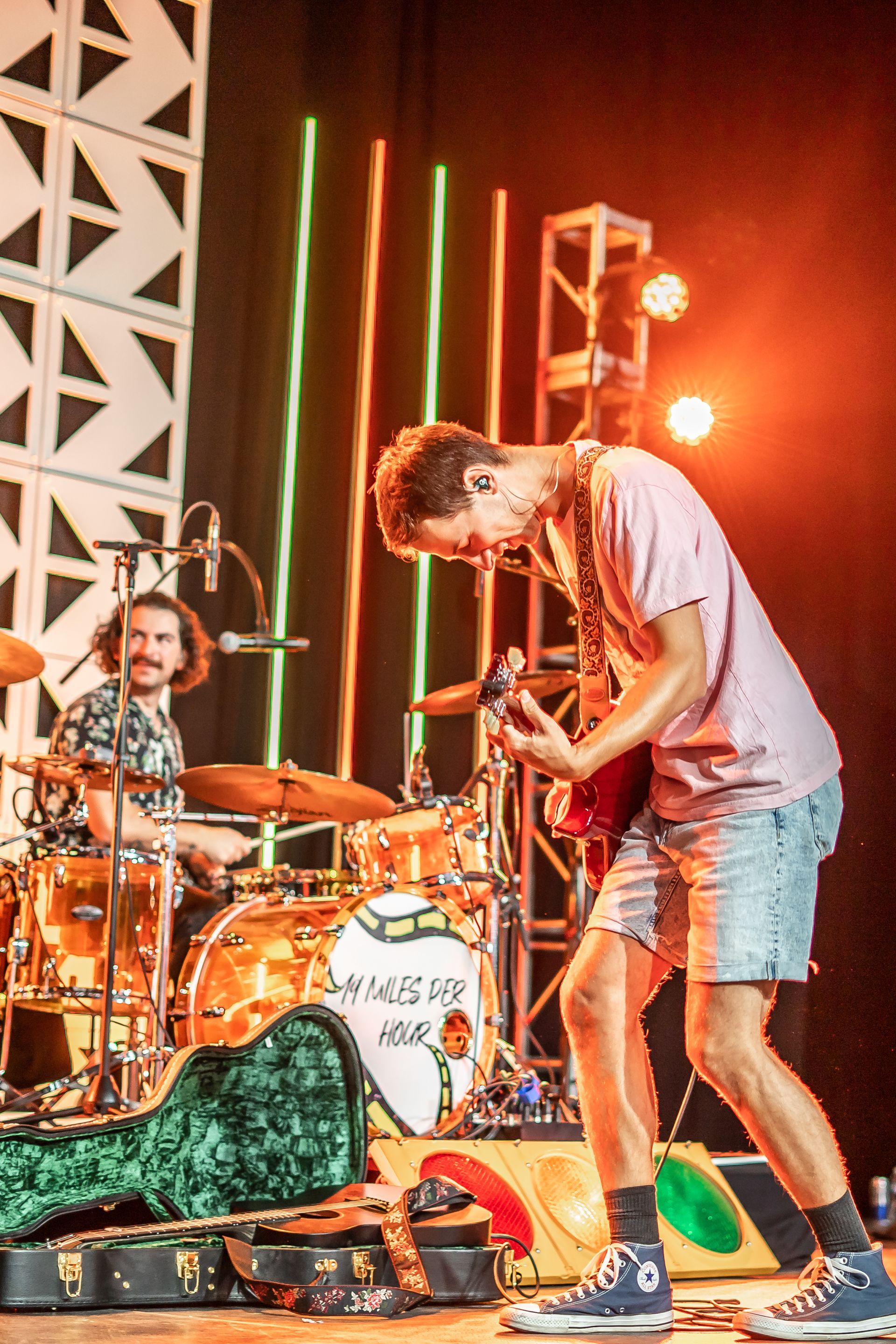 A man is playing a guitar on a stage in front of a drum set.