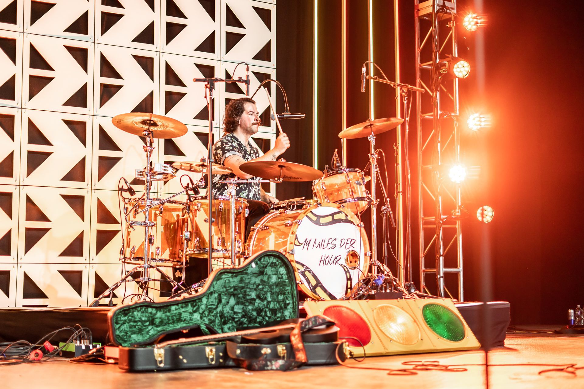 A man is playing drums on a stage with a guitar in the foreground.