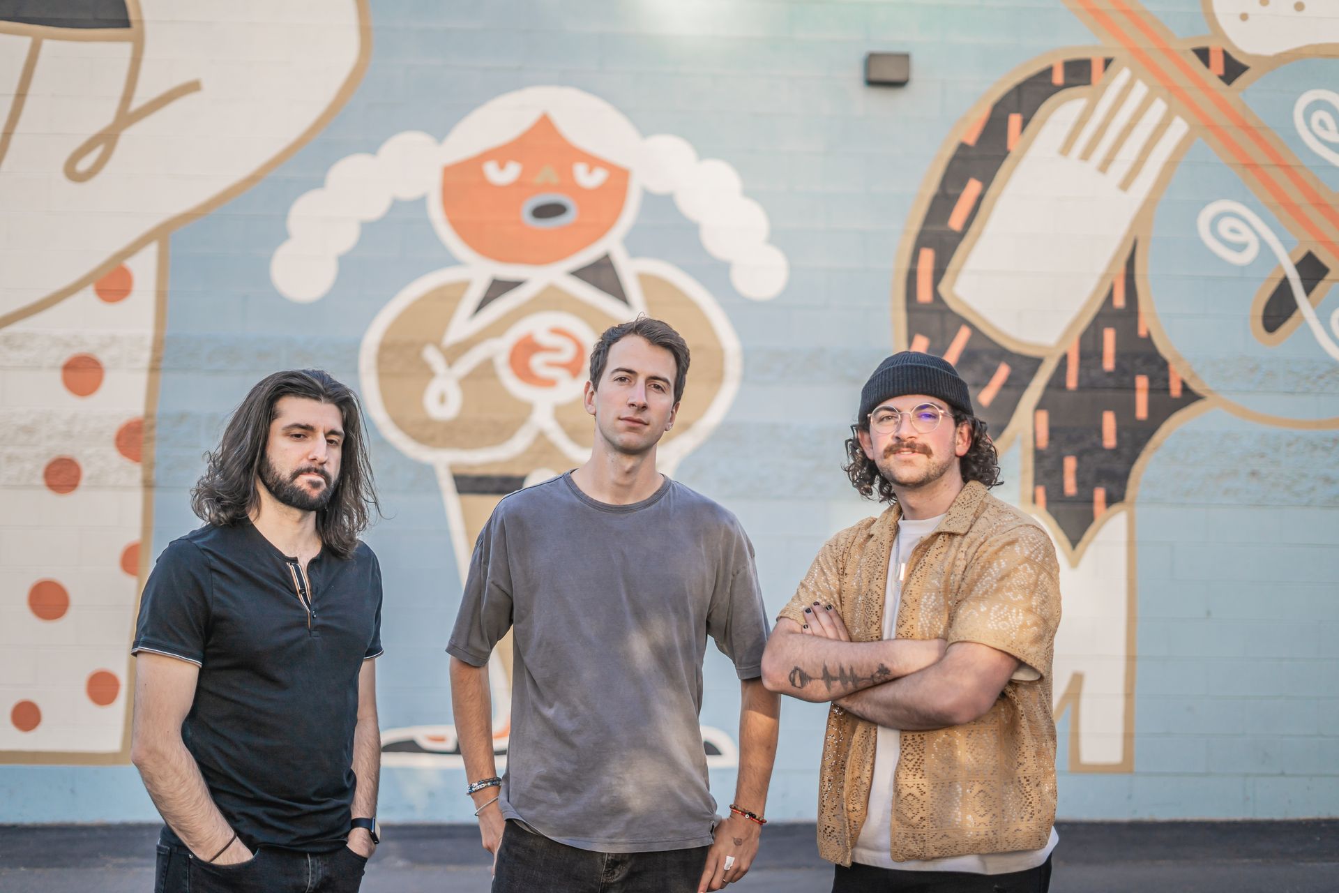Three men are standing in front of a mural on a wall.