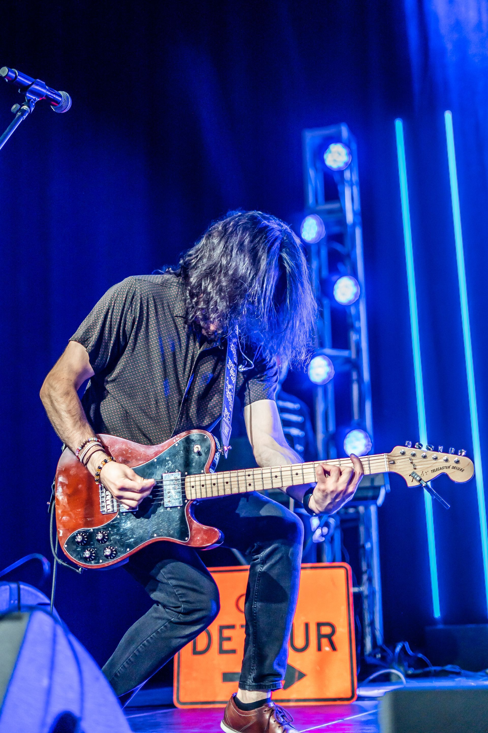 A man is playing a guitar on a stage in front of a detour sign.