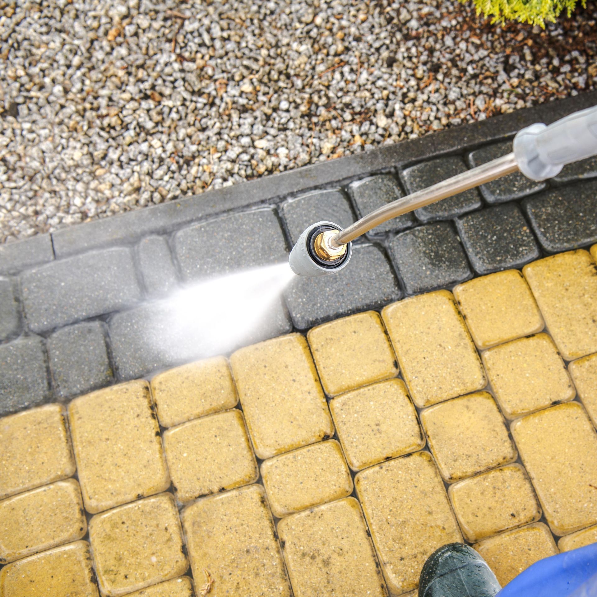 Close-up of a worker performing a pressure washing service on a driveway's bricks.