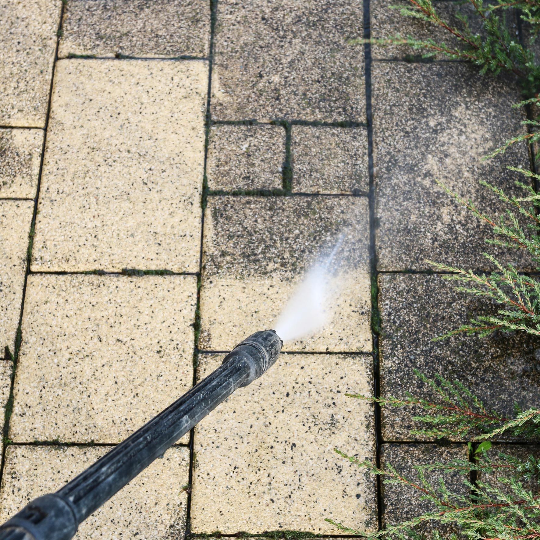 An unrecognized person is pressure washing brick pavers outside a residential home.