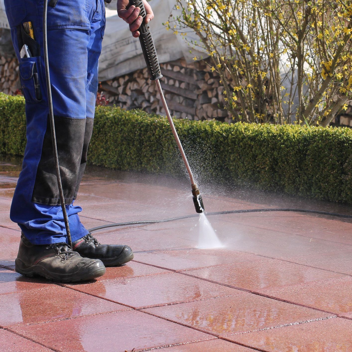 Worker pressure washing patio pavers for professional driveway and outdoor surface cleaning services.