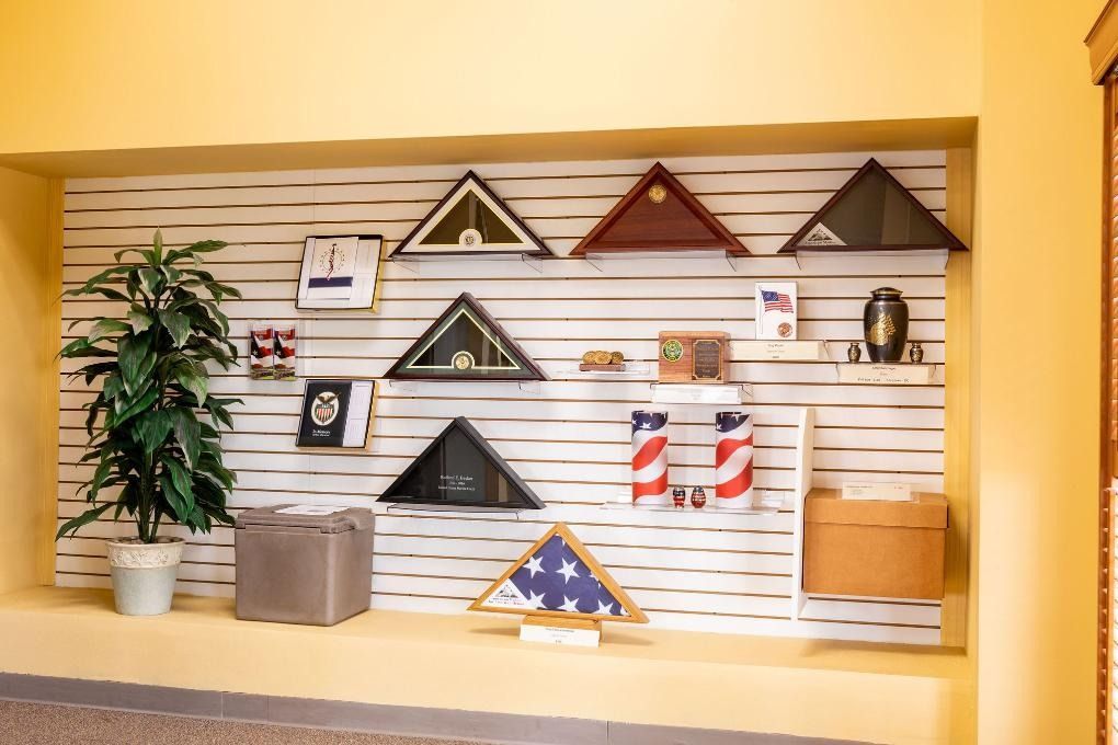 Display of memorial items, including flag cases, urns, and other tributes, arranged on shelves.