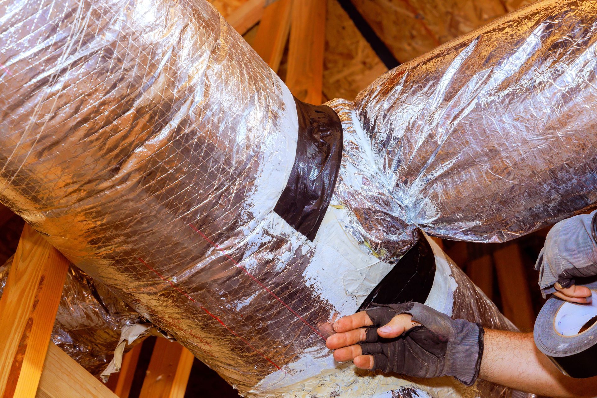 Insulated HVAC ducts with a worker’s gloved hand in an attic-like wooden space