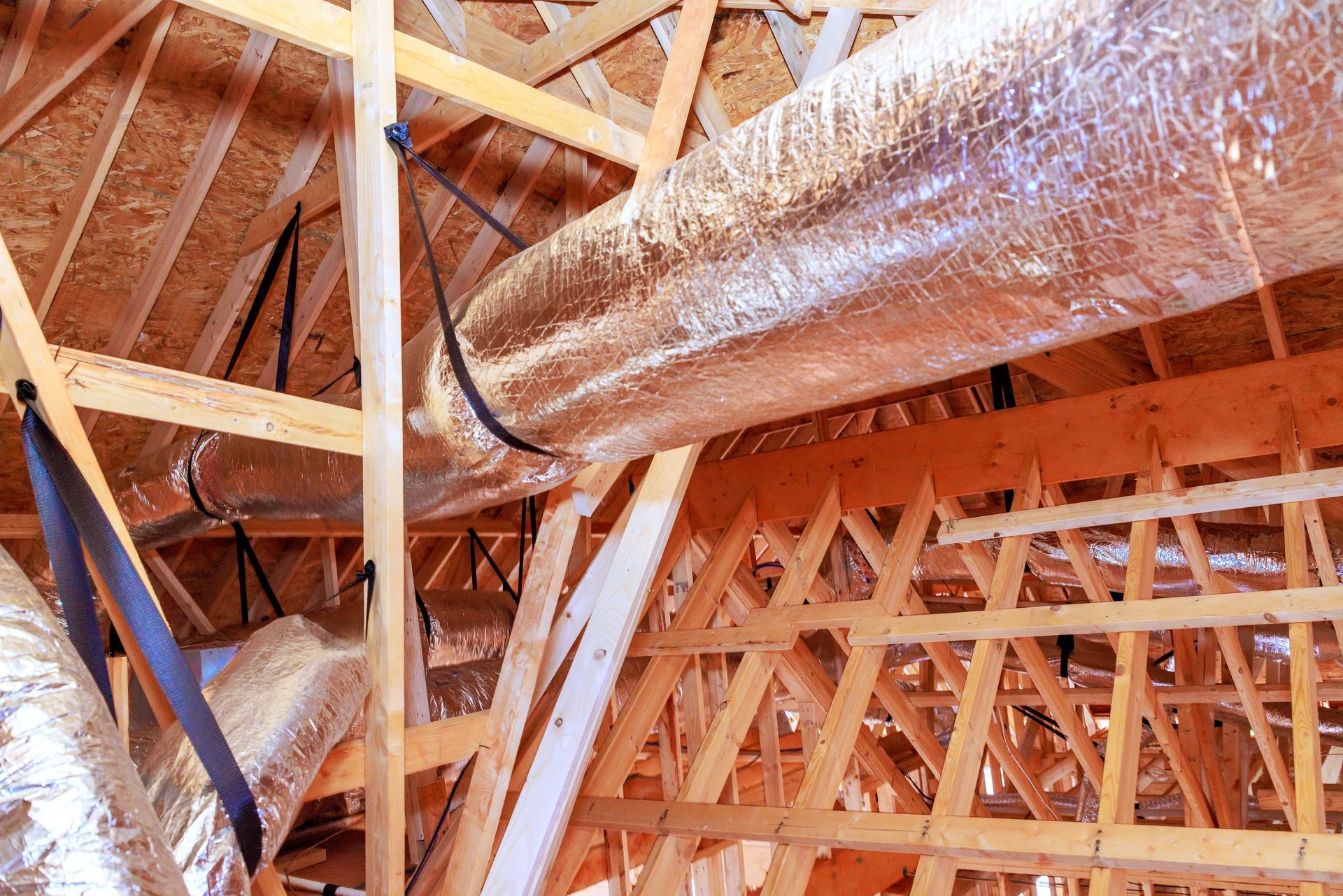 Attic framing with exposed wooden trusses and silver insulated ducts under a roof