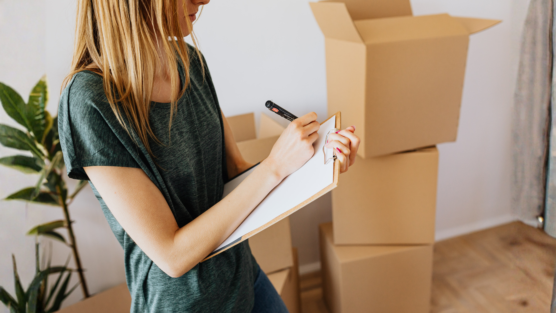 Person completing a maintenance checklist on a clipboard near stacked cardboard boxes.