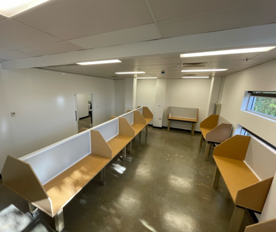 Empty office with rows of tan study pods, white walls, and overhead fluorescent lights Empty office with rows of tan study pods, white walls, and overhead fluorescent lights