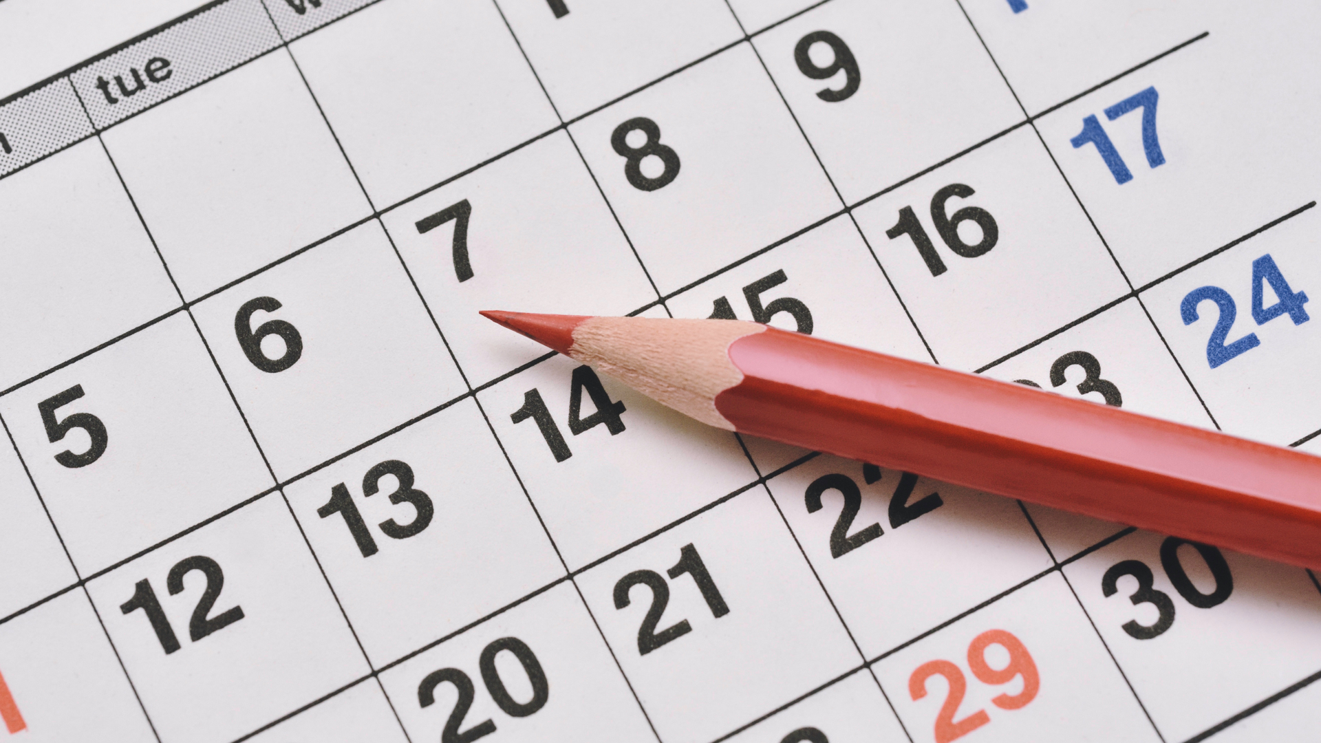 Close-up of a calendar page with a red pencil pointing at dates.