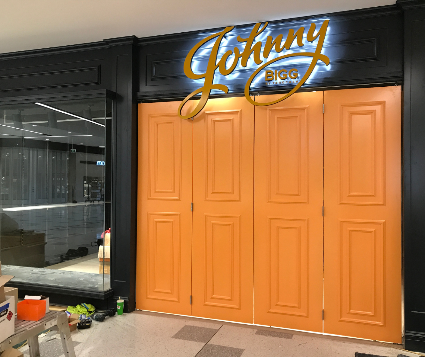 Orange double doors beneath a glowing “Johnny” sign in a modern storefront corridor