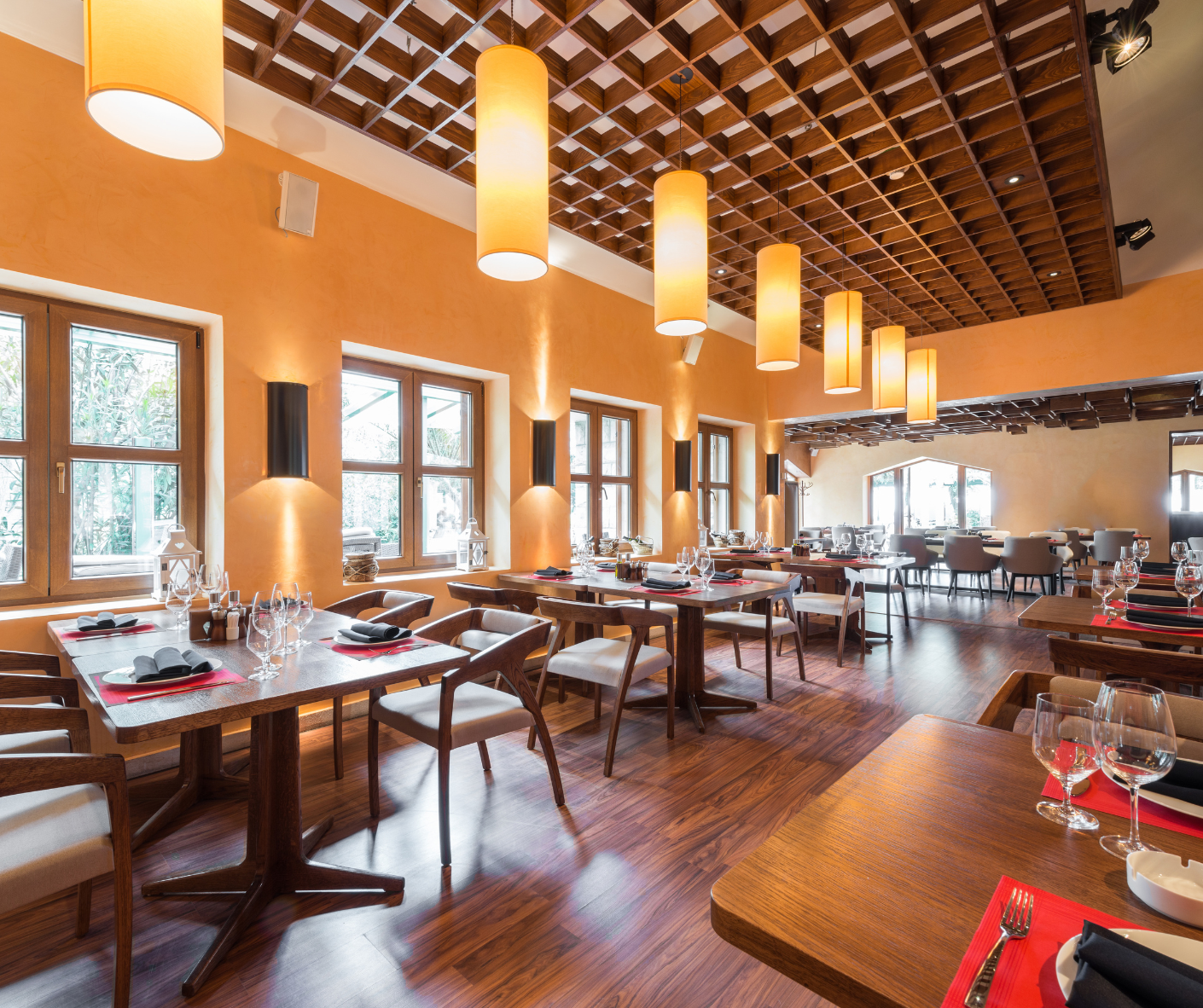 Bright restaurant dining room with wooden tables, hanging pendant lights, and large windows over hardwood floors Bright restaurant dining room with wooden tables, hanging pendant lights, and large windows over hardwood floors