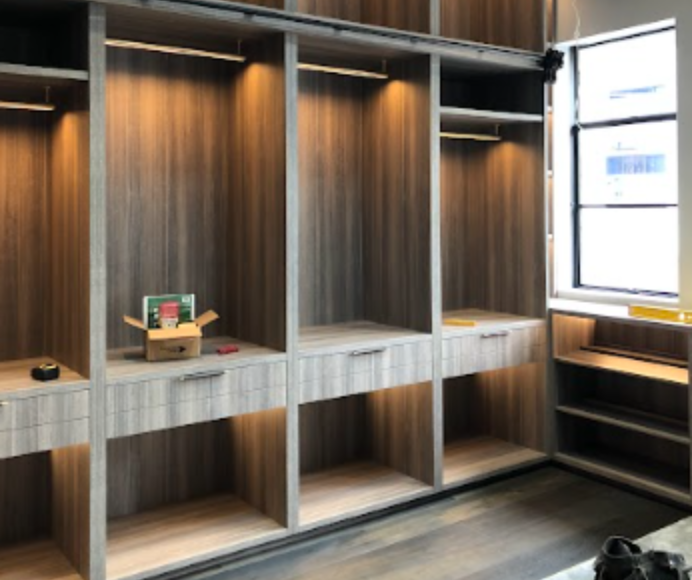 Built-in wooden cubby shelves with drawers in a modern room beside a bright window.