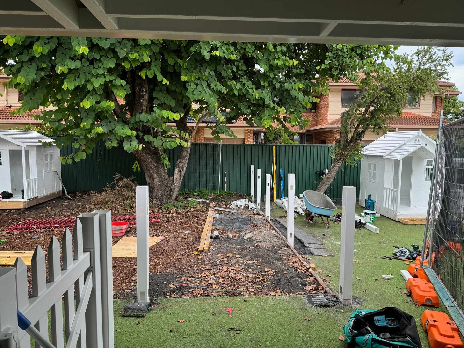 A backyard with a fence , sheds , and a tree.