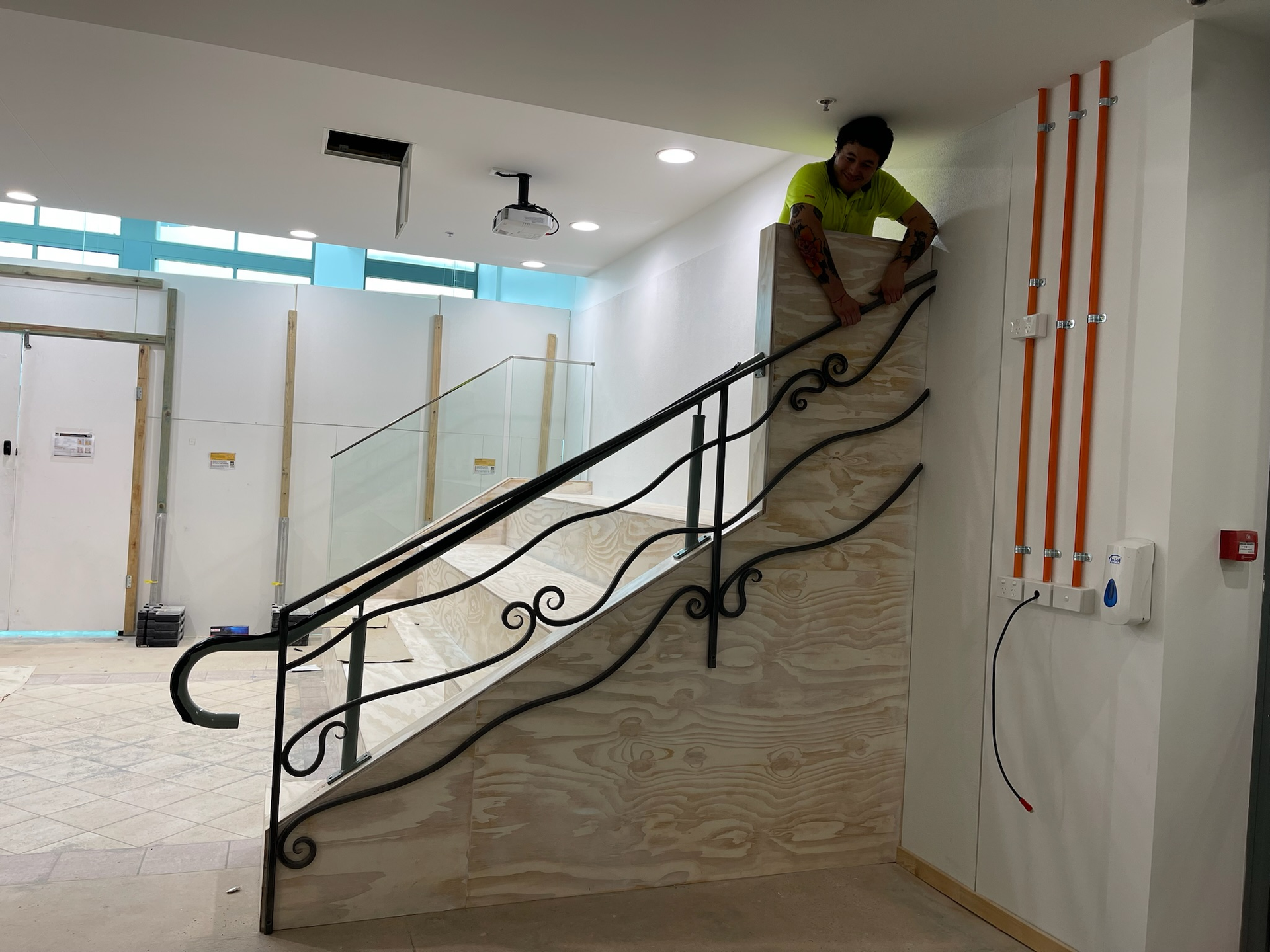 Commercial builder installing a decorative black handrail on an internal timber staircase during a Brisbane office fitout.
