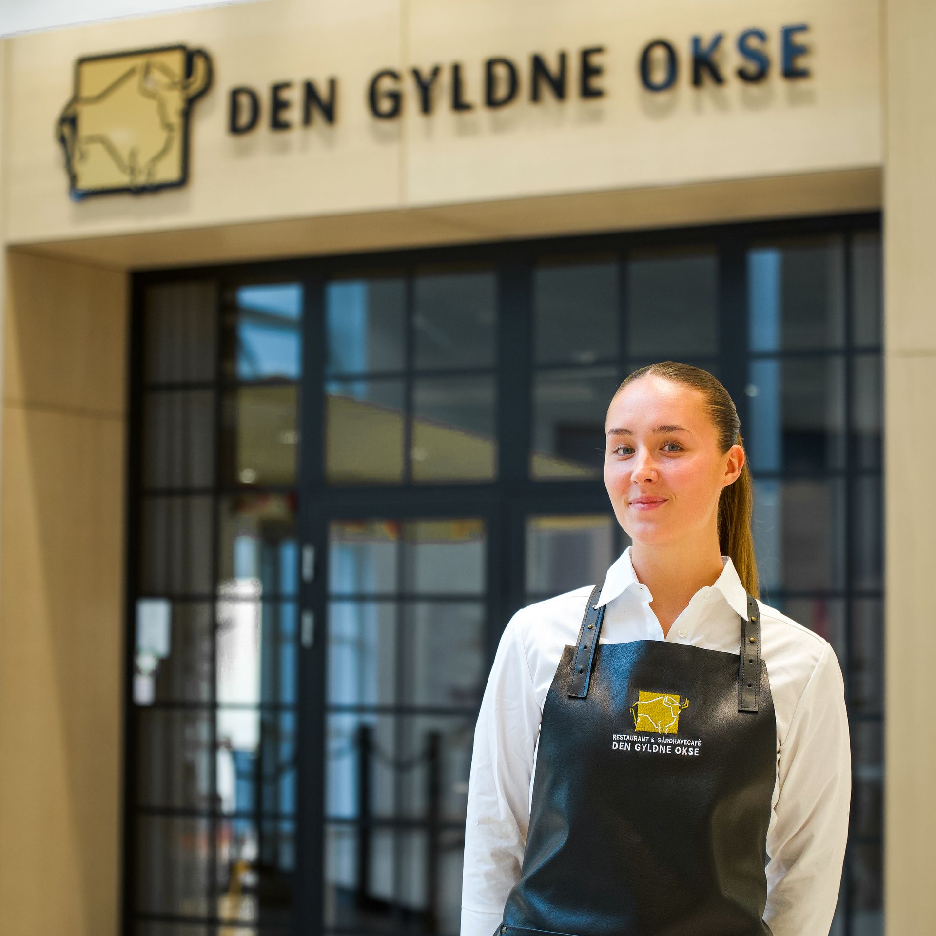 Kvinde i sort forklæde står foran indgangen til restauranten 