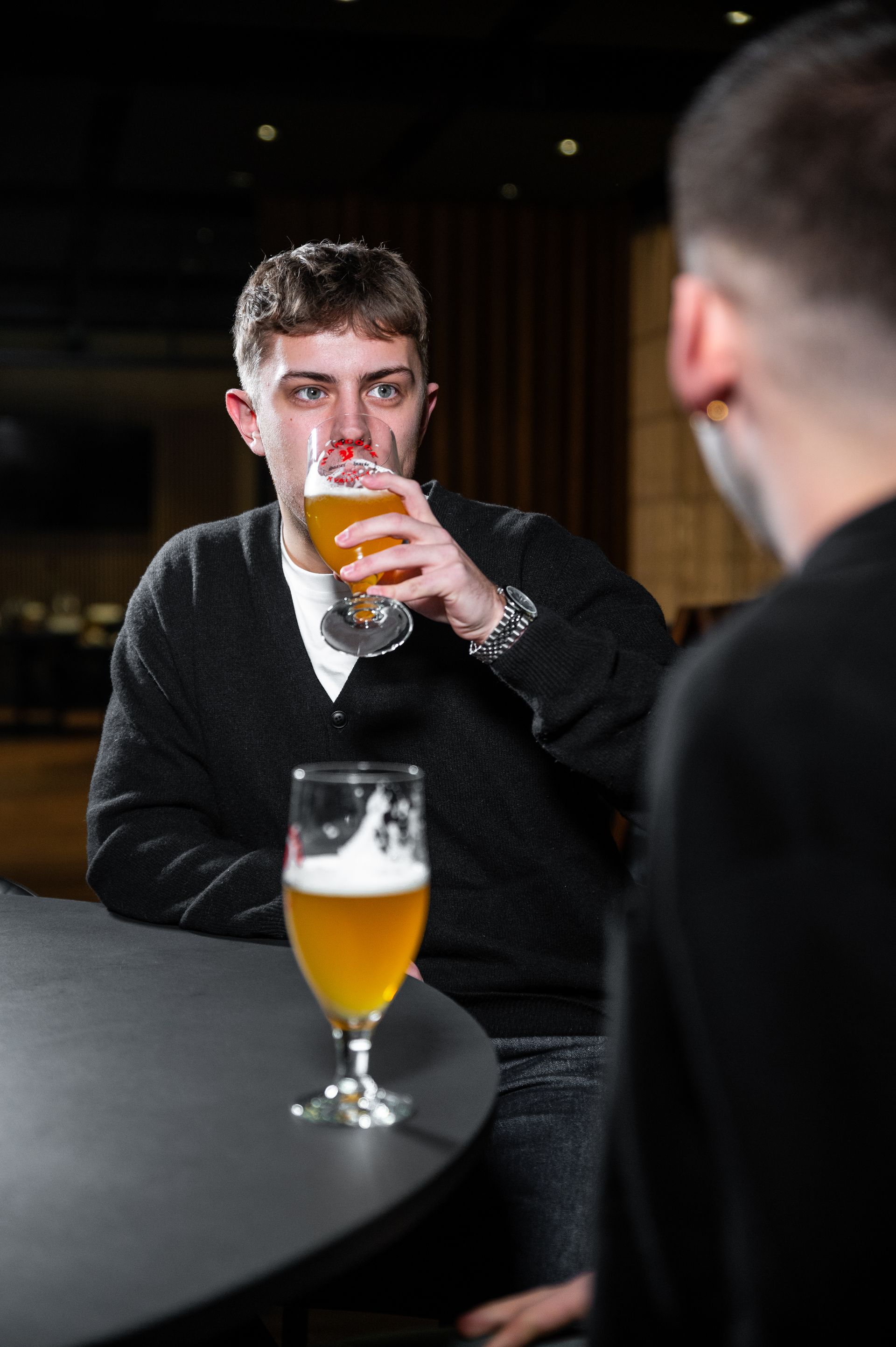 To mænd på en mørk bar; den ene drikker øl, den anden sidder overfor ham.