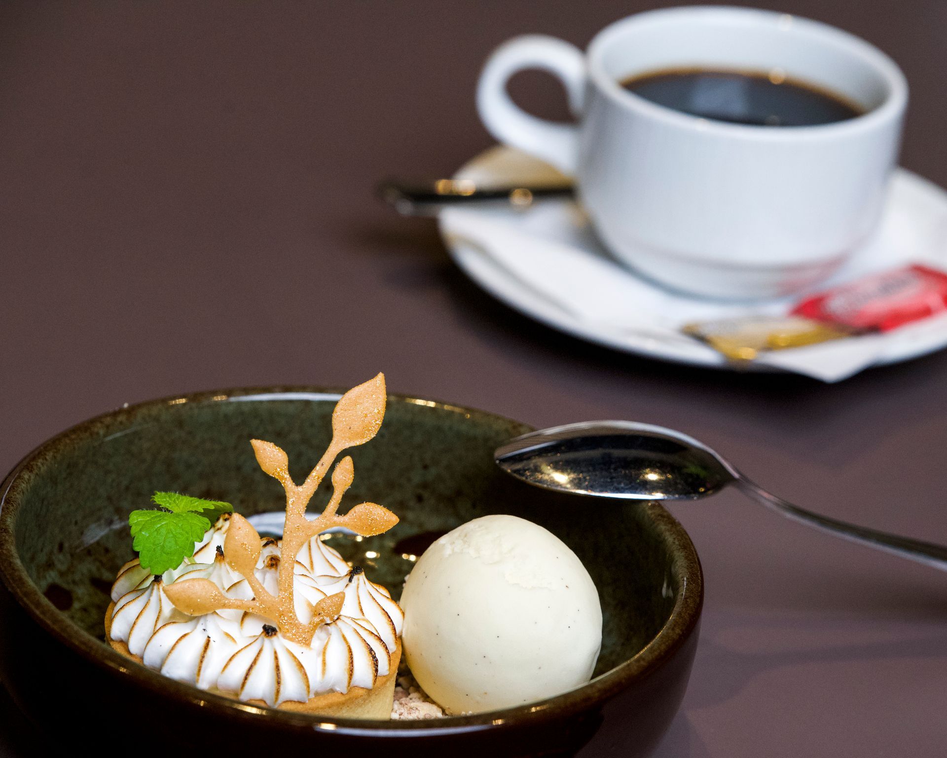 Dessertskål med marengs, is og kaffekop på en brun overflade.