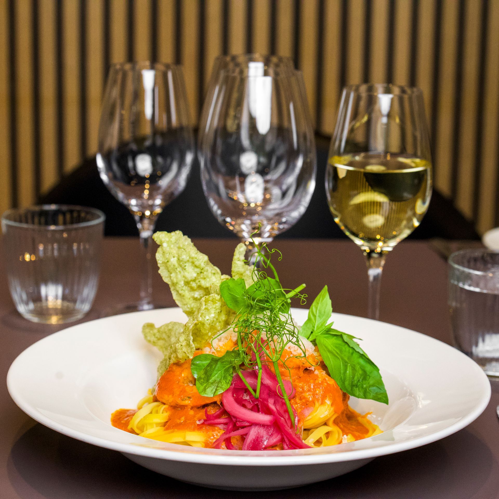 Pastatallerken med fisk, syltede løg og basilikum med tre vinglas.